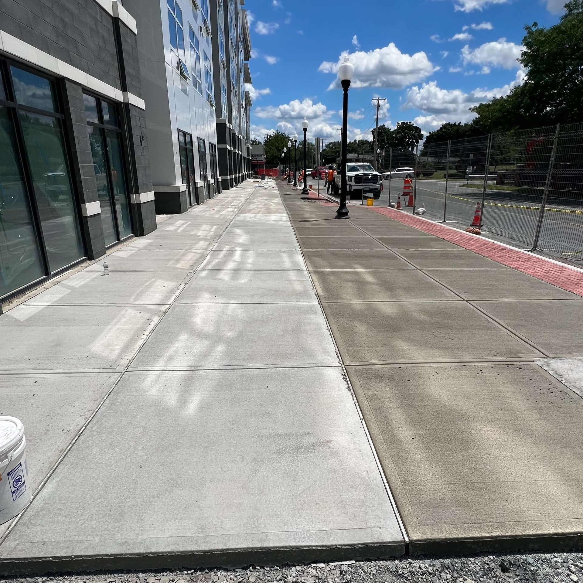 Sidewalk being pressure washed, concrete cleaned; building on left.