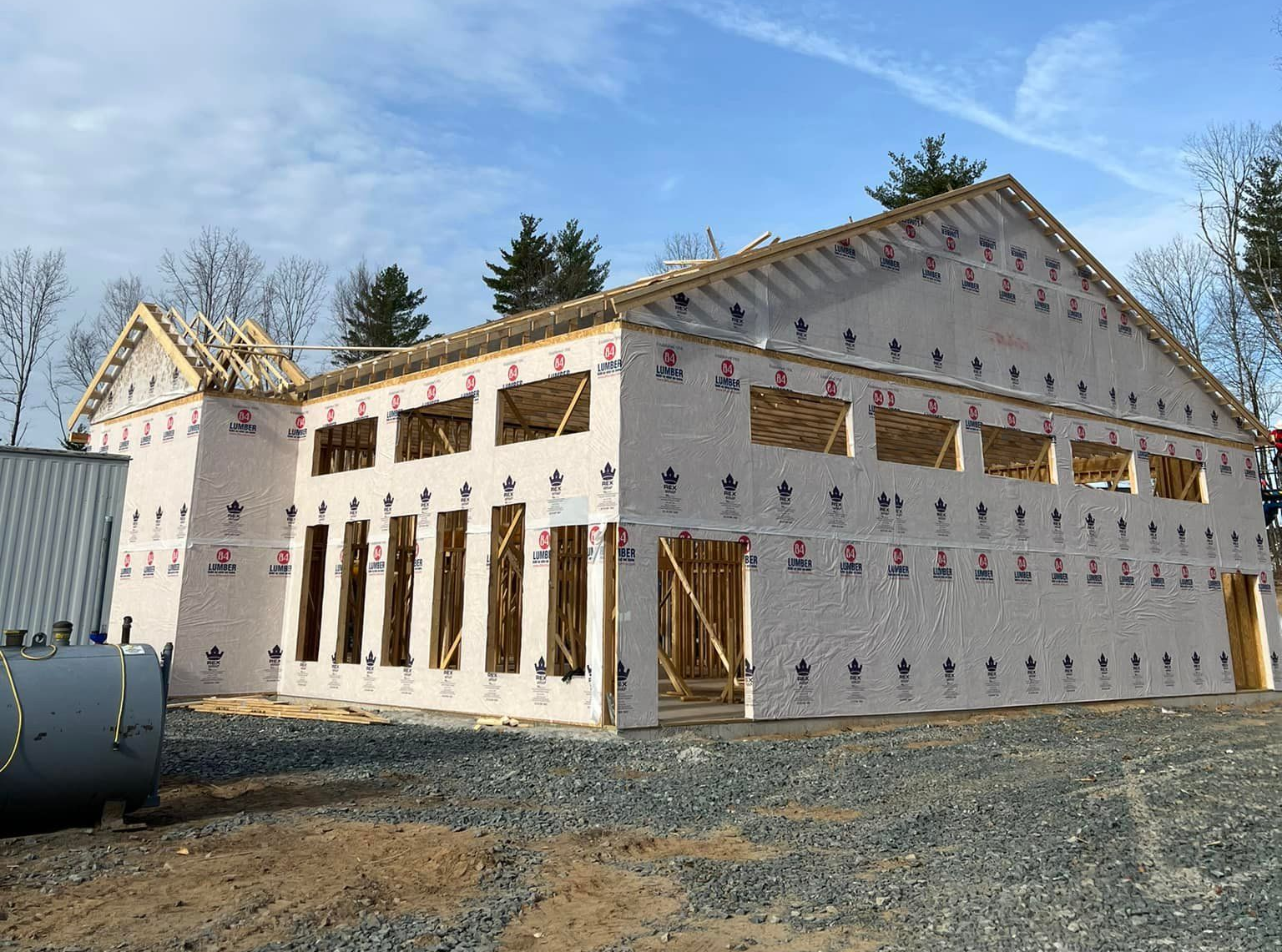 Building under construction, wood frame with white sheathing, windows, and roof supports against a blue sky.