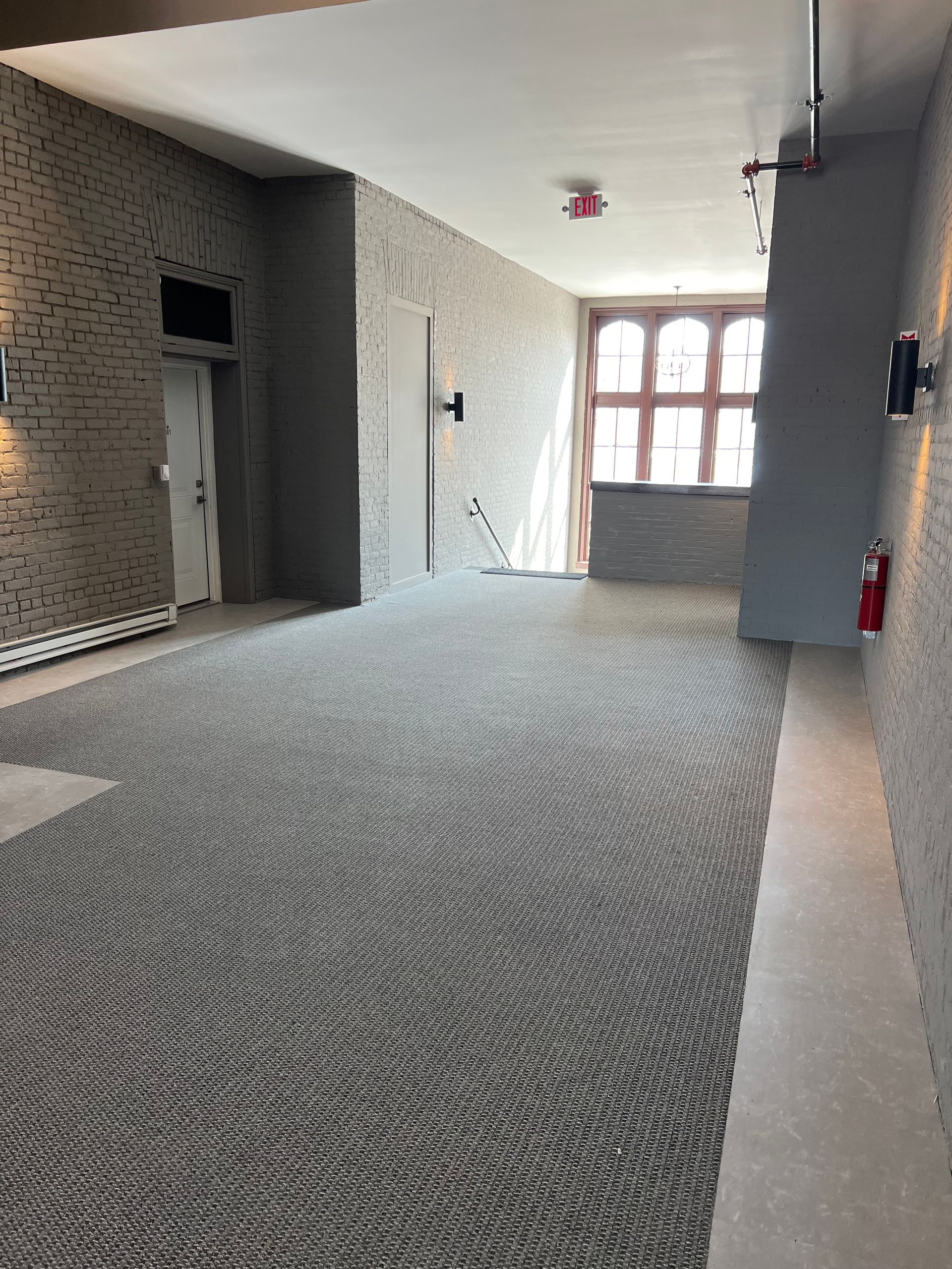 Long hallway with gray carpet, textured walls, and a window at the end.