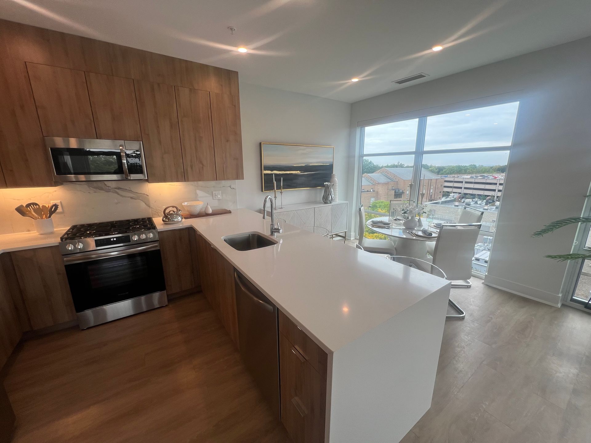 Modern kitchen with light wood cabinets, white countertops, stainless steel appliances, and large windows.