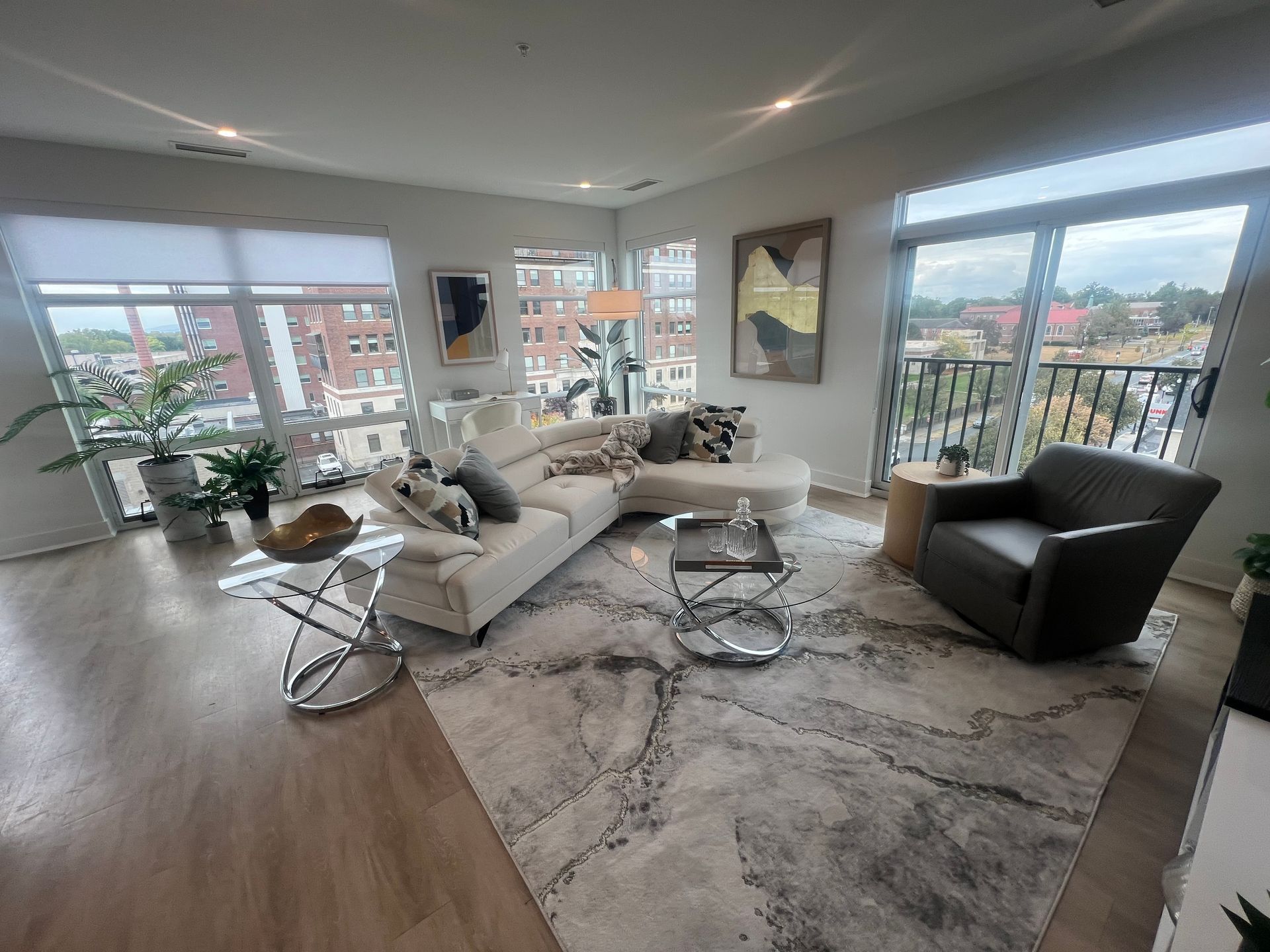 Bright living room with white sectional, rug, and modern decor. Large windows offer city views.