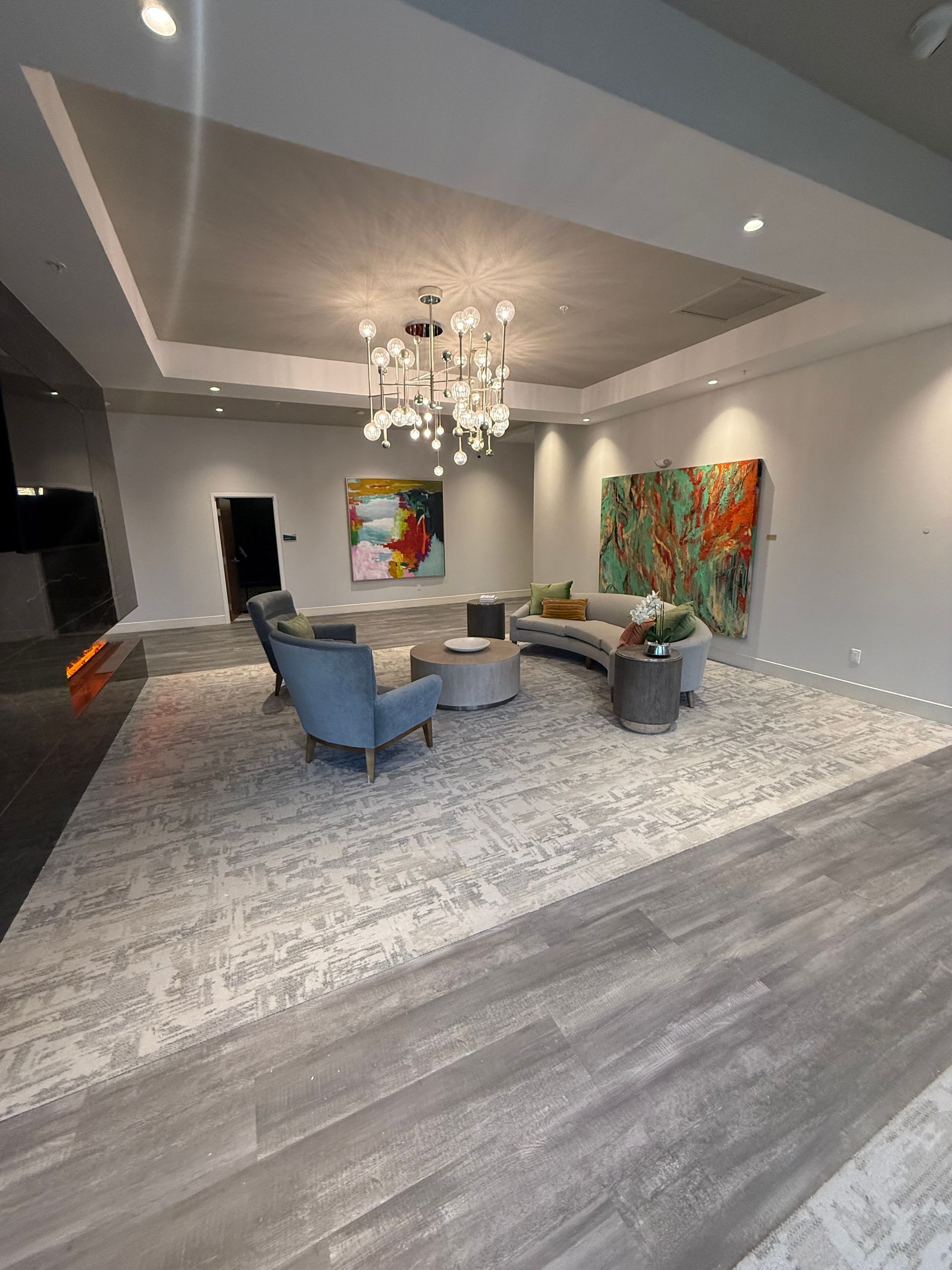 Spacious lobby with seating area, modern art, and chandelier on a large rug over light gray flooring.