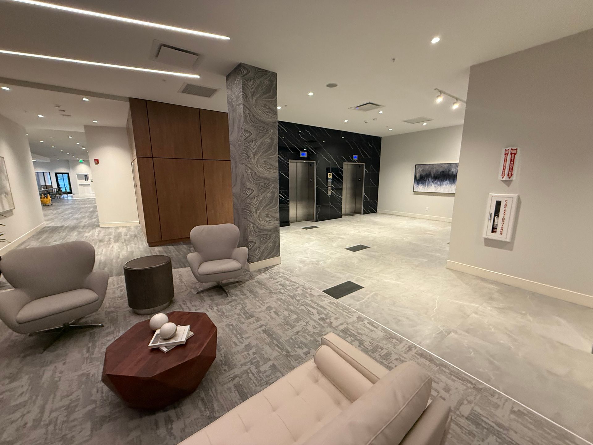 Lobby with seating, elevators, and art. Gray and white color scheme.