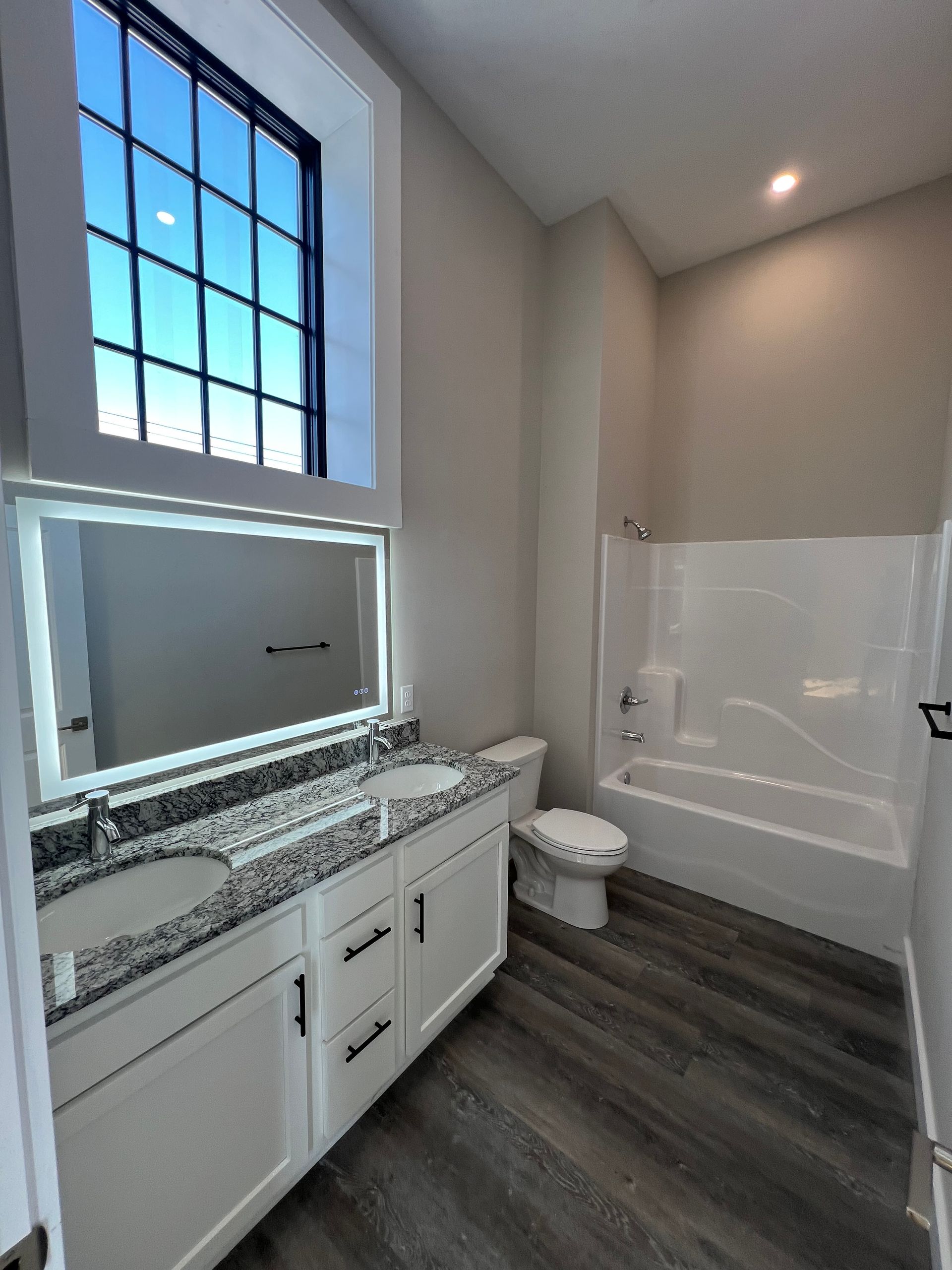 Bathroom with white cabinets, dark countertops, a window, and a bathtub.