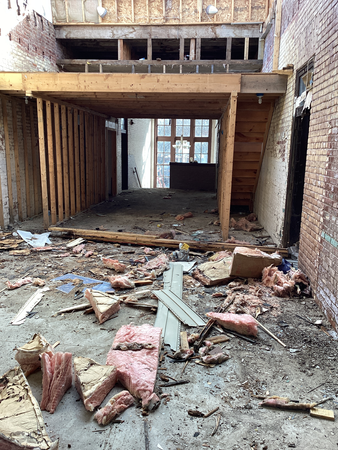Construction site with debris and exposed framing; entrance to another room is visible.