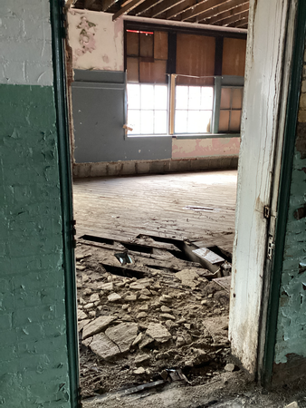 Open doorway into a dilapidated room with damaged floor, peeling paint, and window.