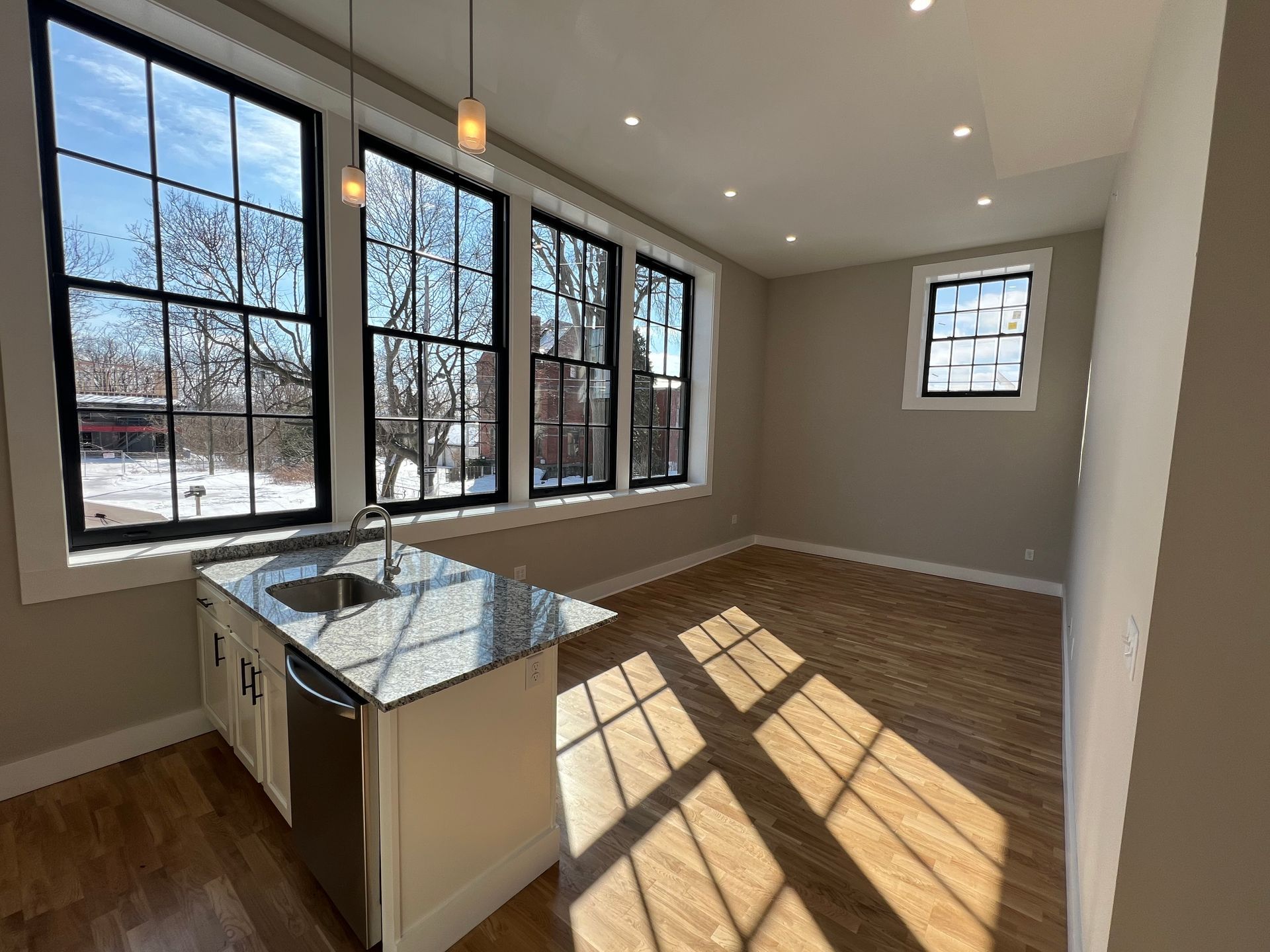 Kitchen with island, black-framed windows, wood floor. Granite countertop, stainless steel sink and appliances. Light-filled room.