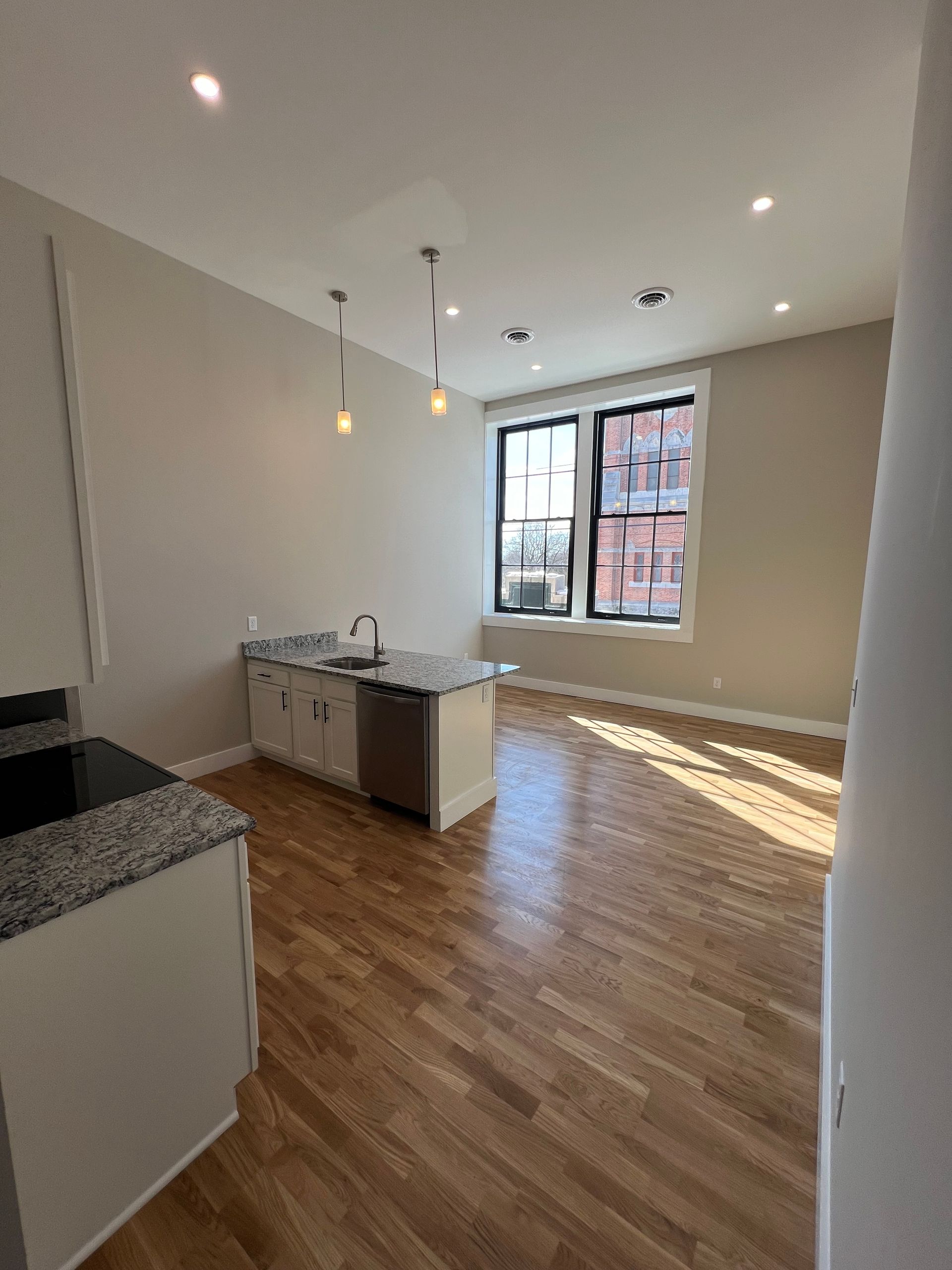 Kitchen with light wood floor, white cabinets, island, and large window.