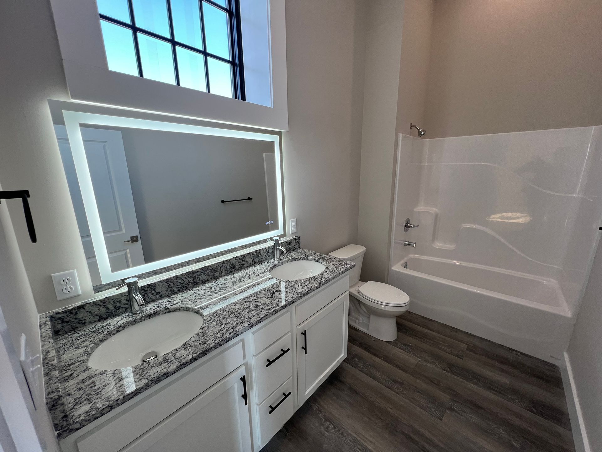 Bathroom with white vanity, double sinks, granite countertop, lighted mirror, and tub.