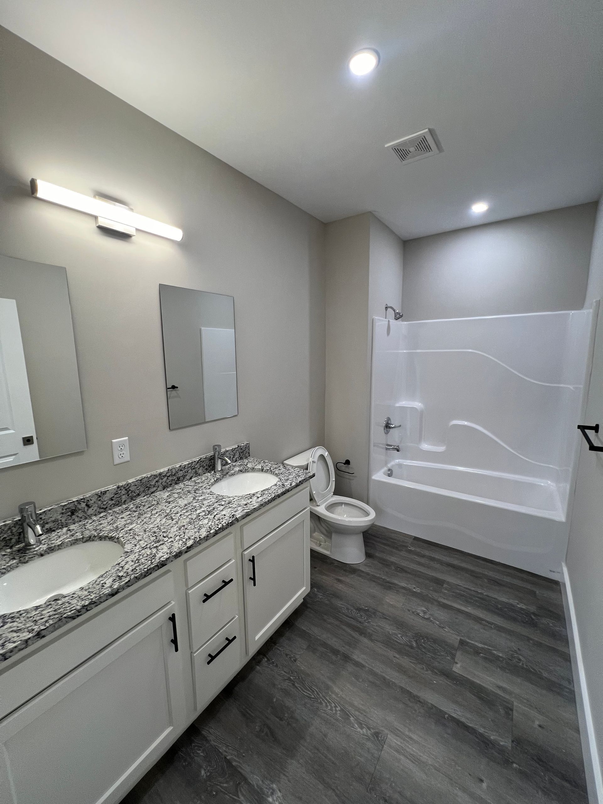 Bathroom with a white vanity, gray countertop, and gray wood-look flooring. White tub/shower combo.