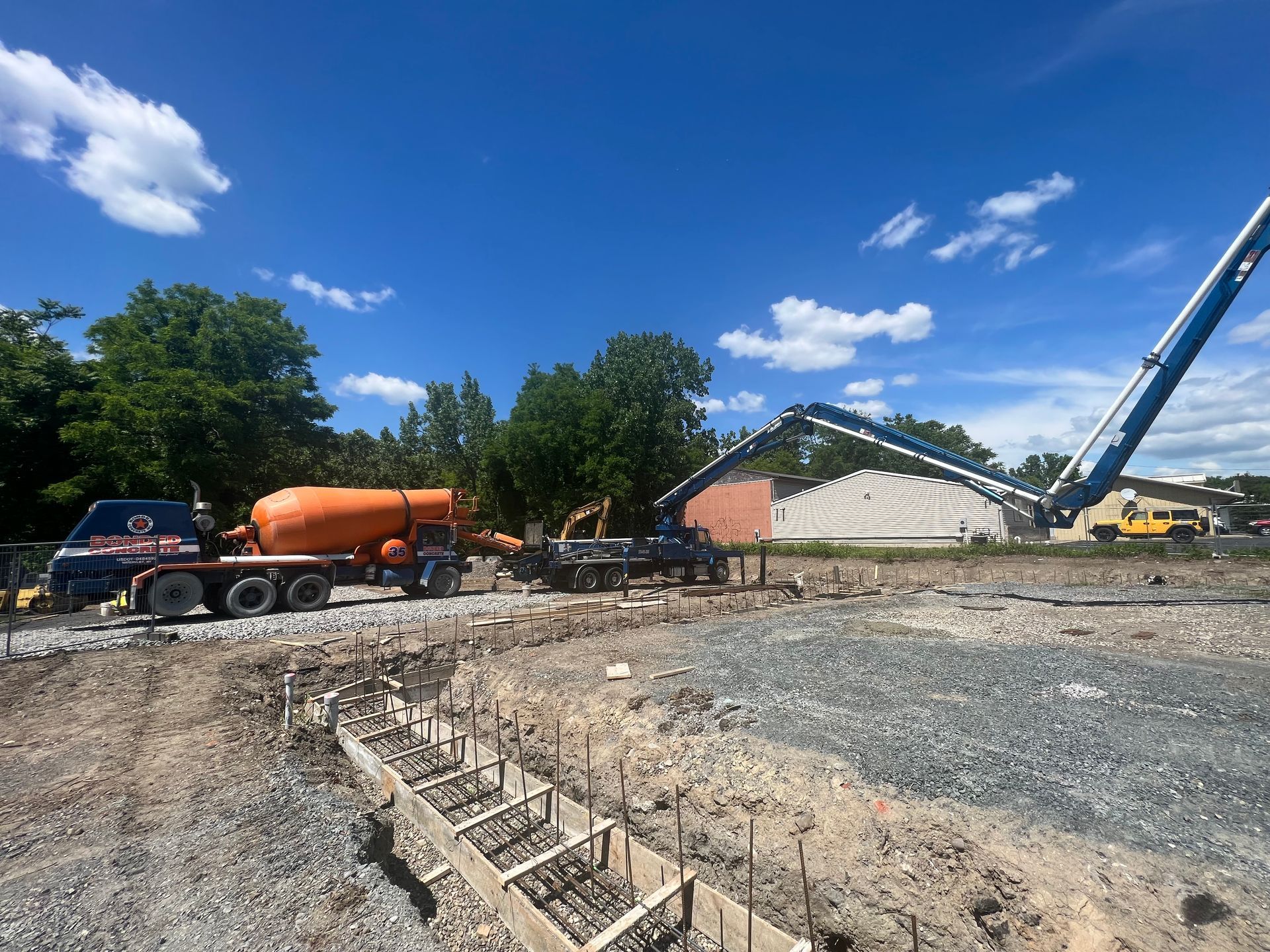 Construction site with concrete truck pouring cement. Blue sky, trees, and dirt.