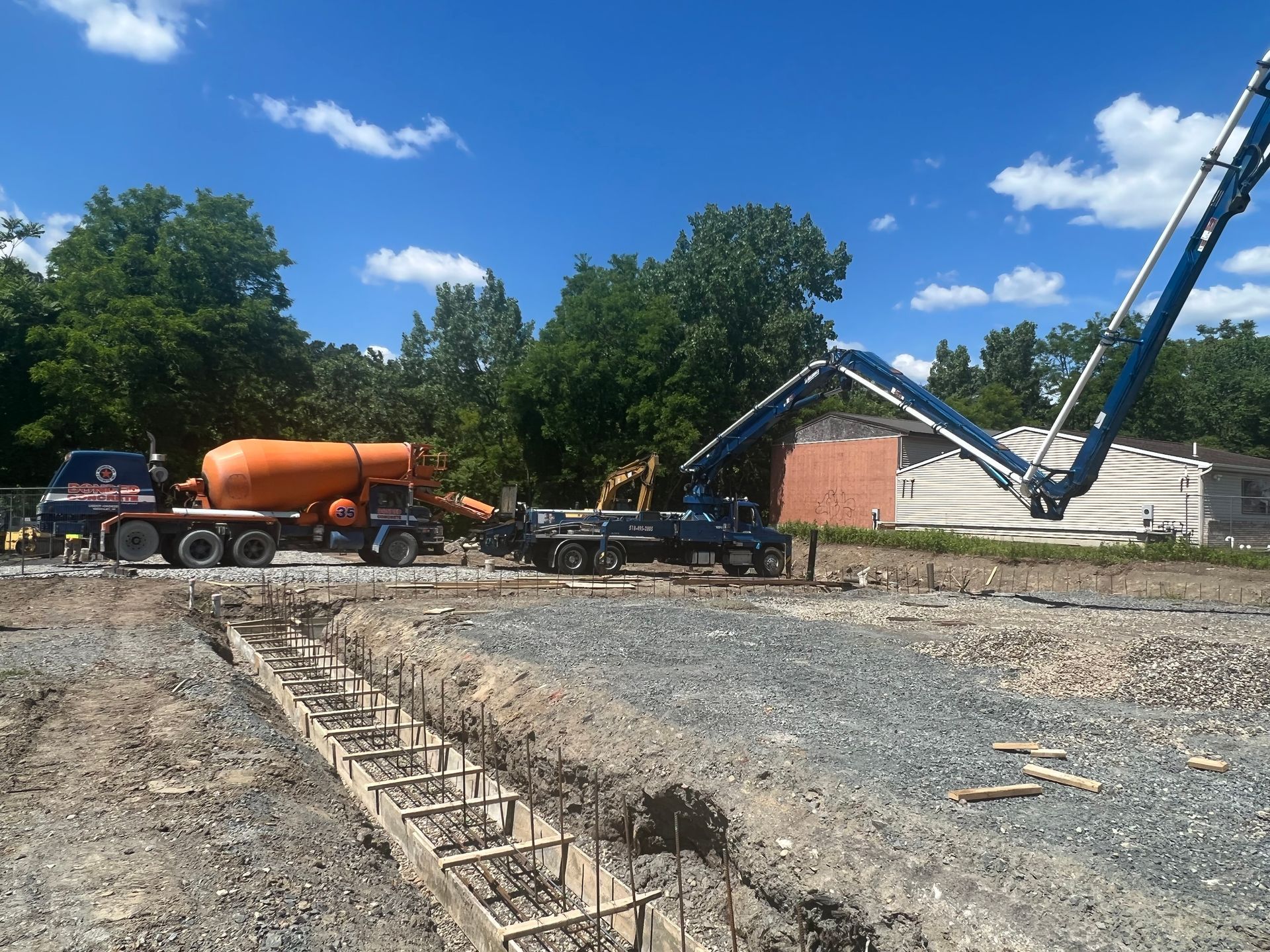 Construction site with cement trucks and a concrete foundation. Blue sky, trees, and gravel.