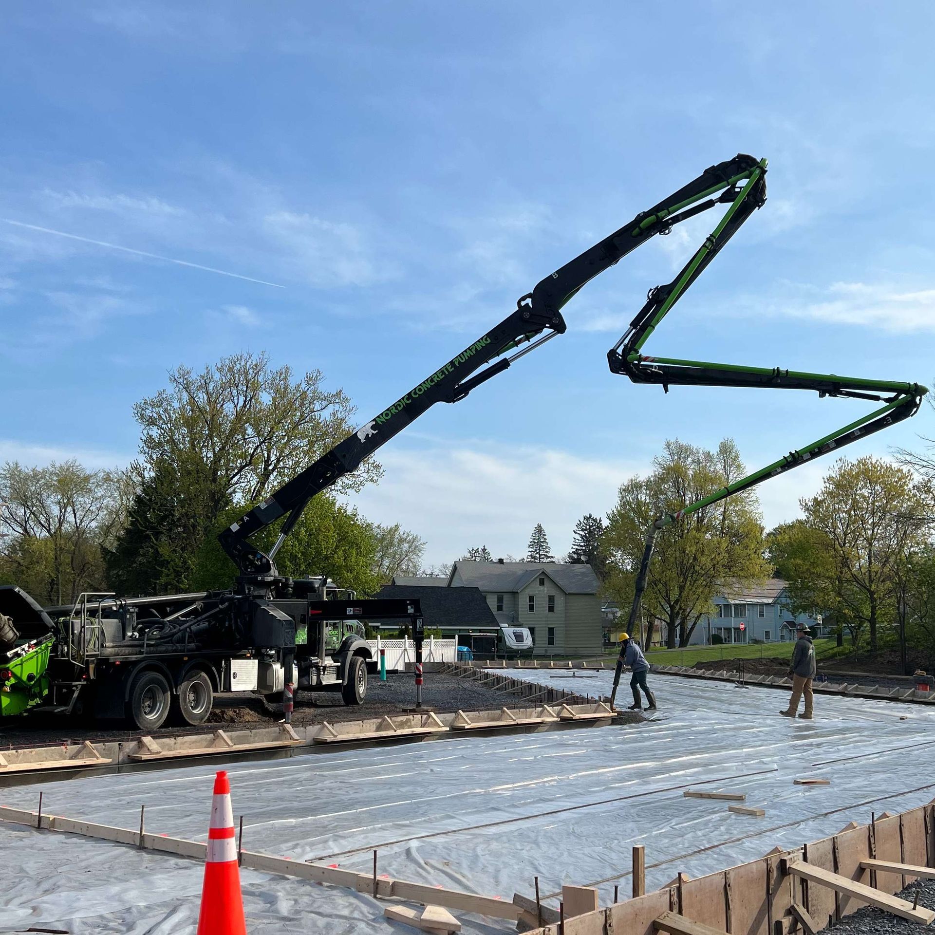 Concrete truck pumping concrete onto a construction site. Two workers leveling concrete; blue sky.