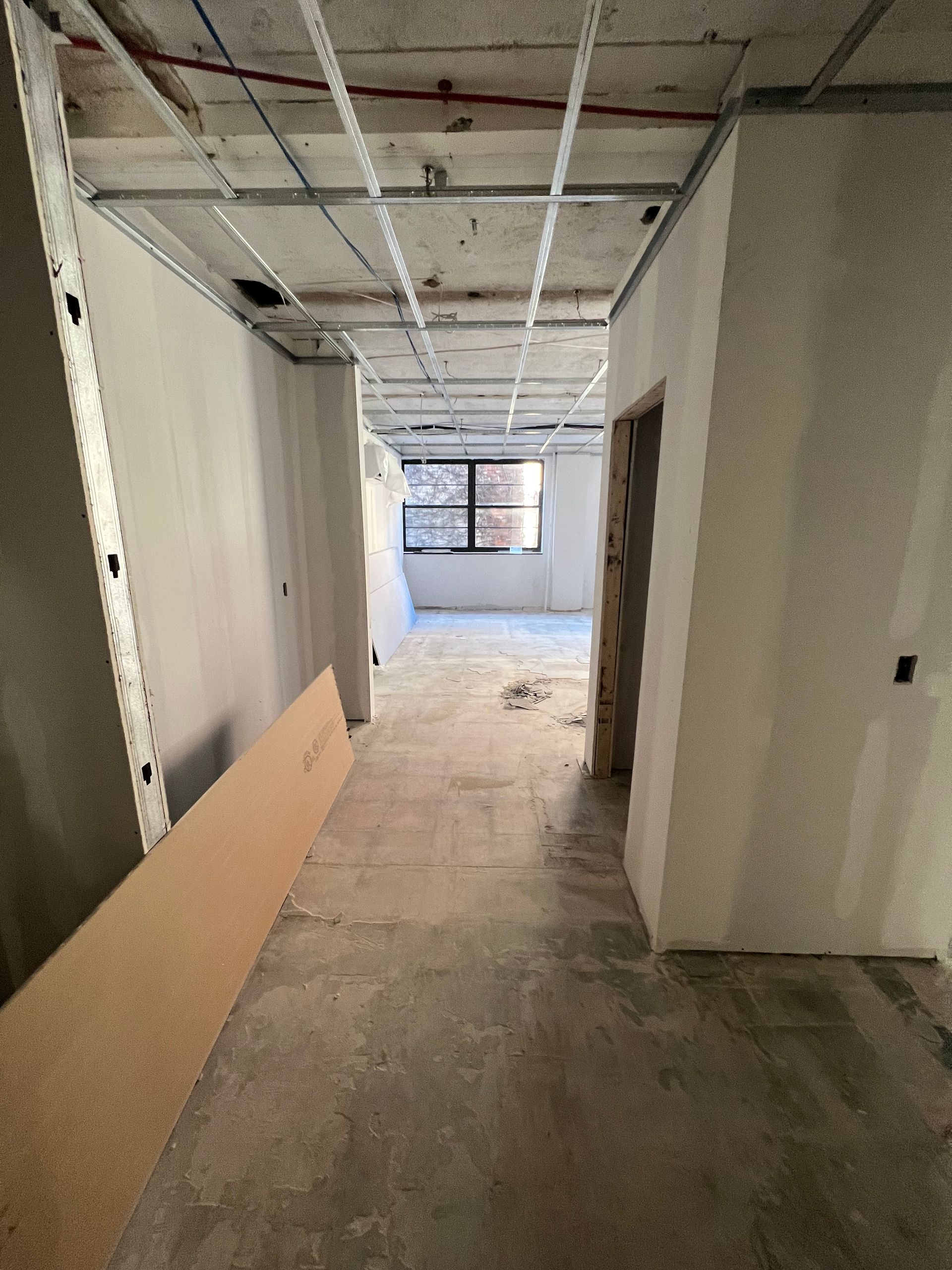 Hallway under construction, unfinished walls and ceiling, concrete floor, open doorways.