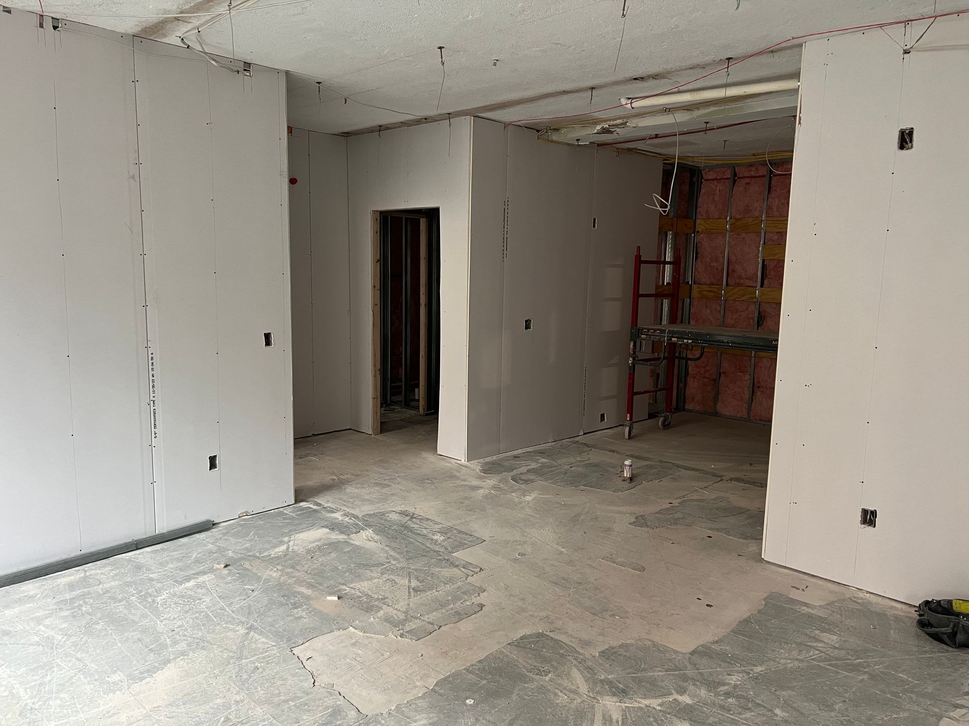 Interior under construction; drywall installation, doorway, open space.