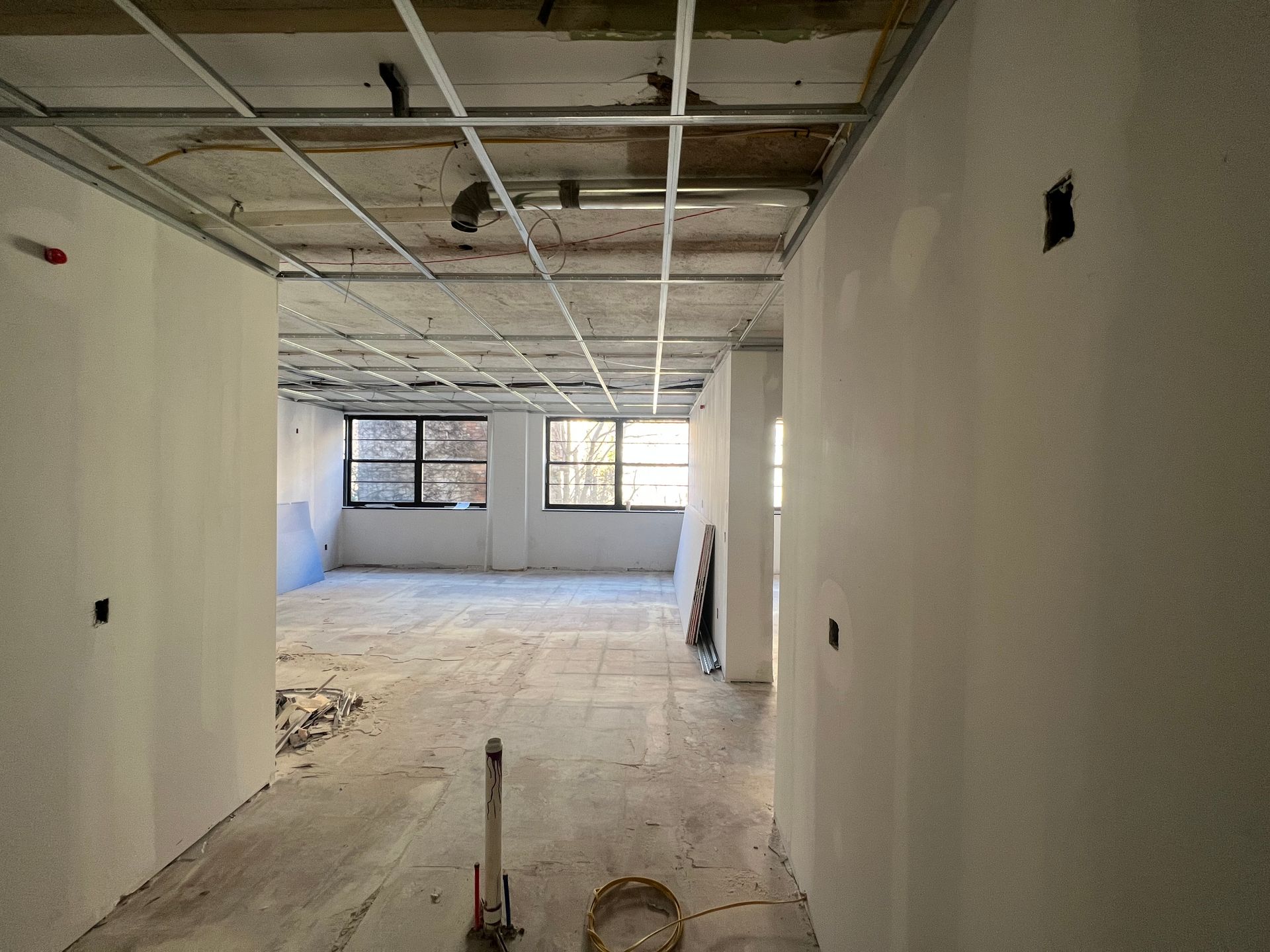 Interior construction: hallway with unfinished walls, exposed ceiling grid, and windows at the end of the room.