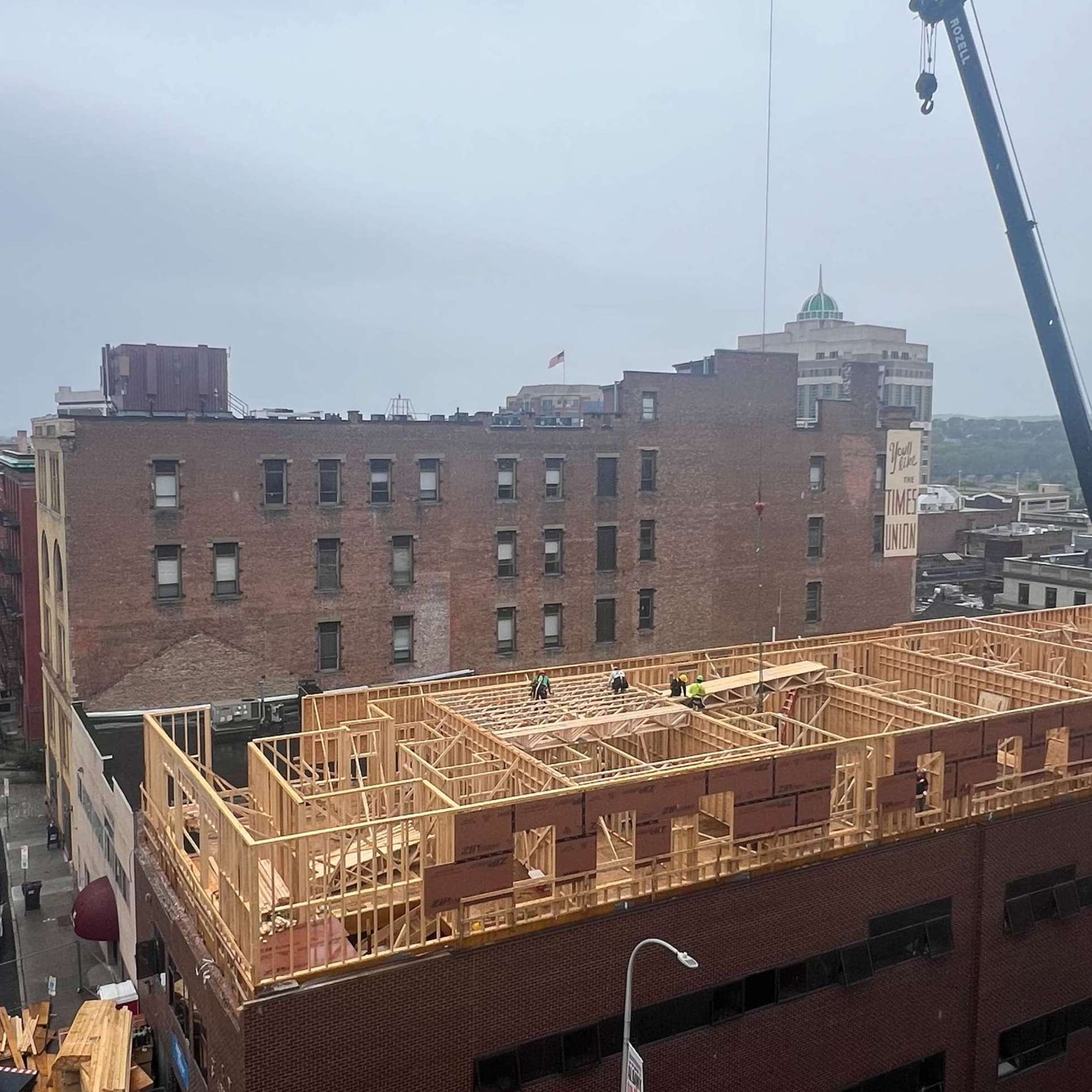 Construction site: wooden frames being built on a brick building with a crane nearby.