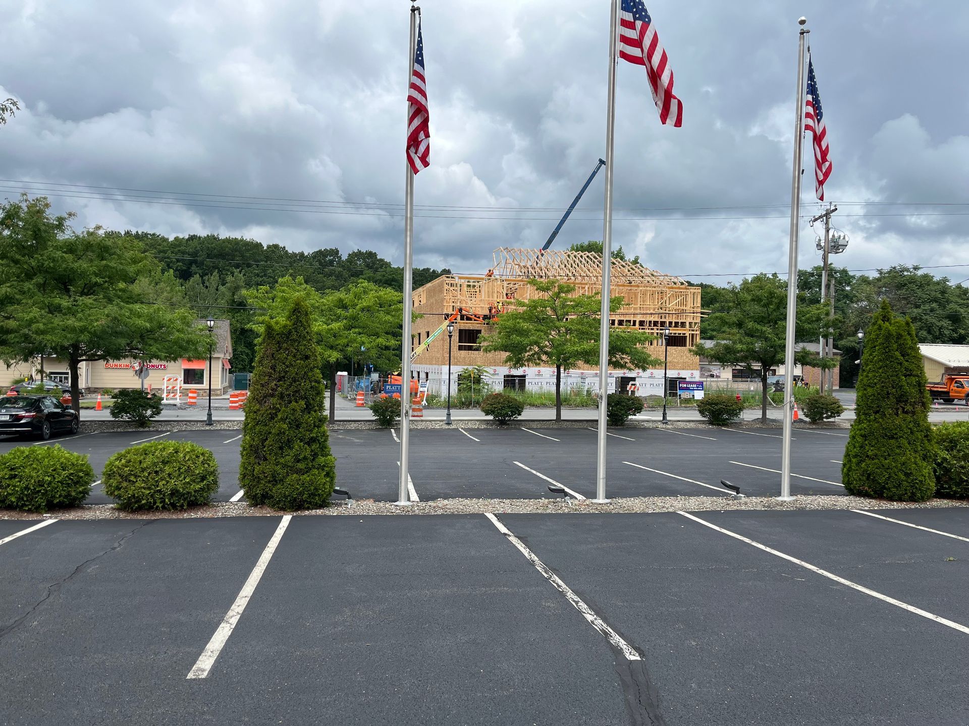 Parking lot with three American flags, trees, and a building under construction on a cloudy day.