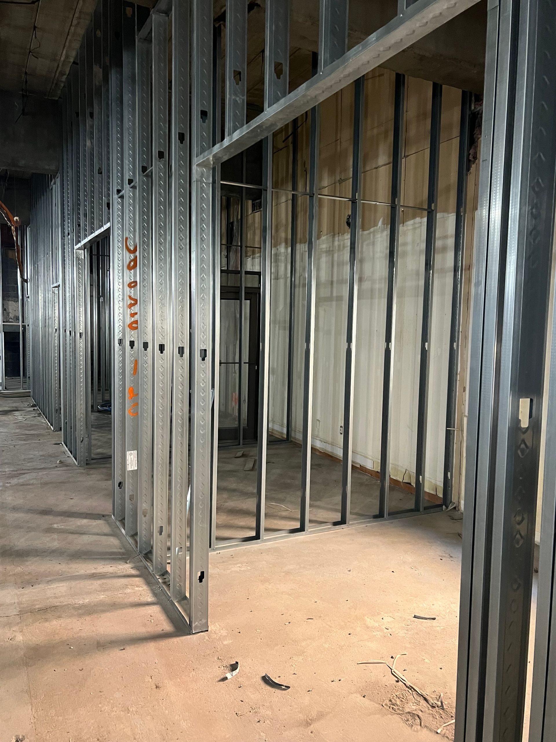 Metal studs framing an interior space during construction; concrete wall in background.