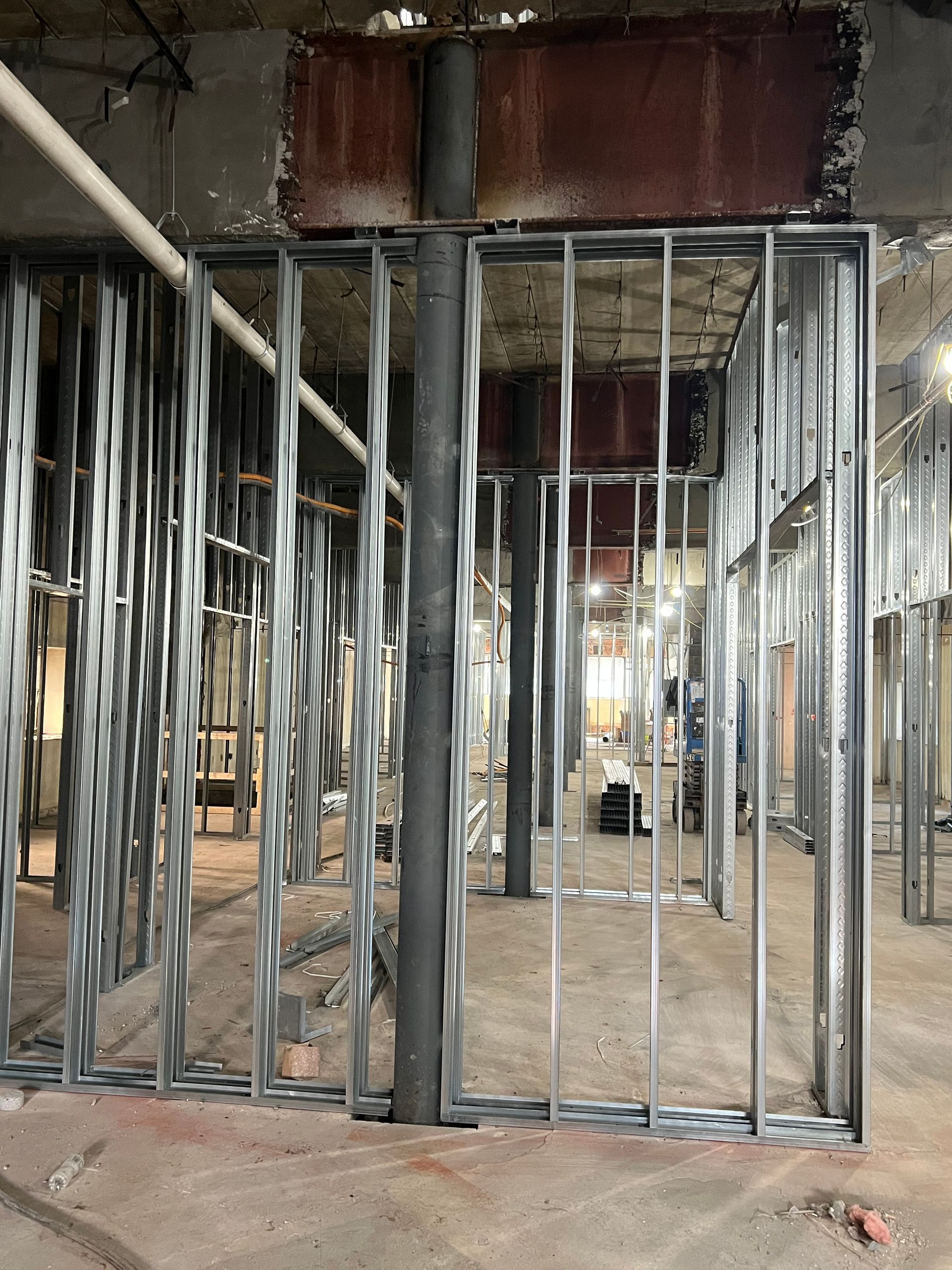 Metal studs frame a construction site's interior walls around a large pipe. The floor is concrete.