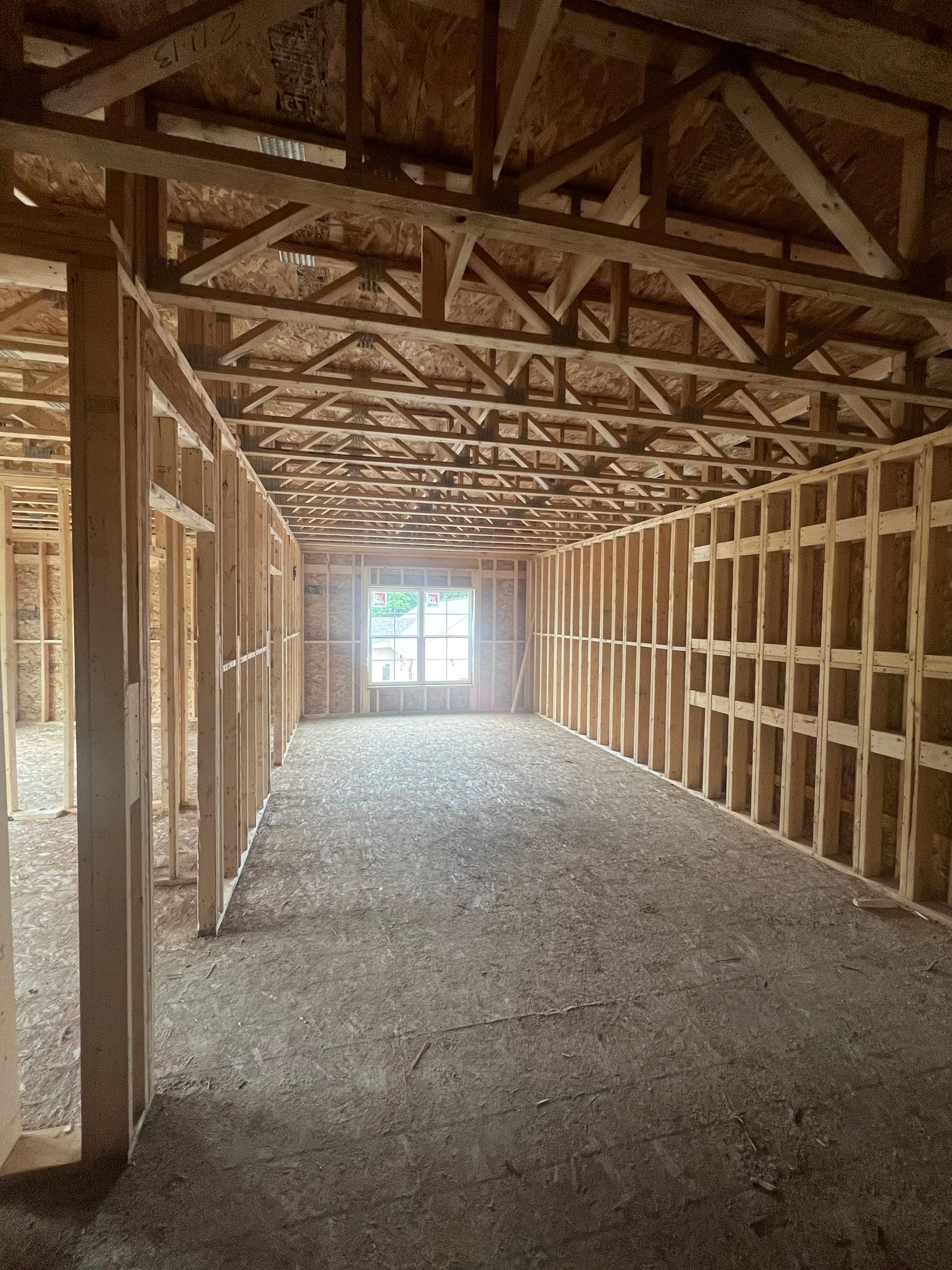 Interior of a building under construction, showing wooden frame walls and ceiling, with window at the end.