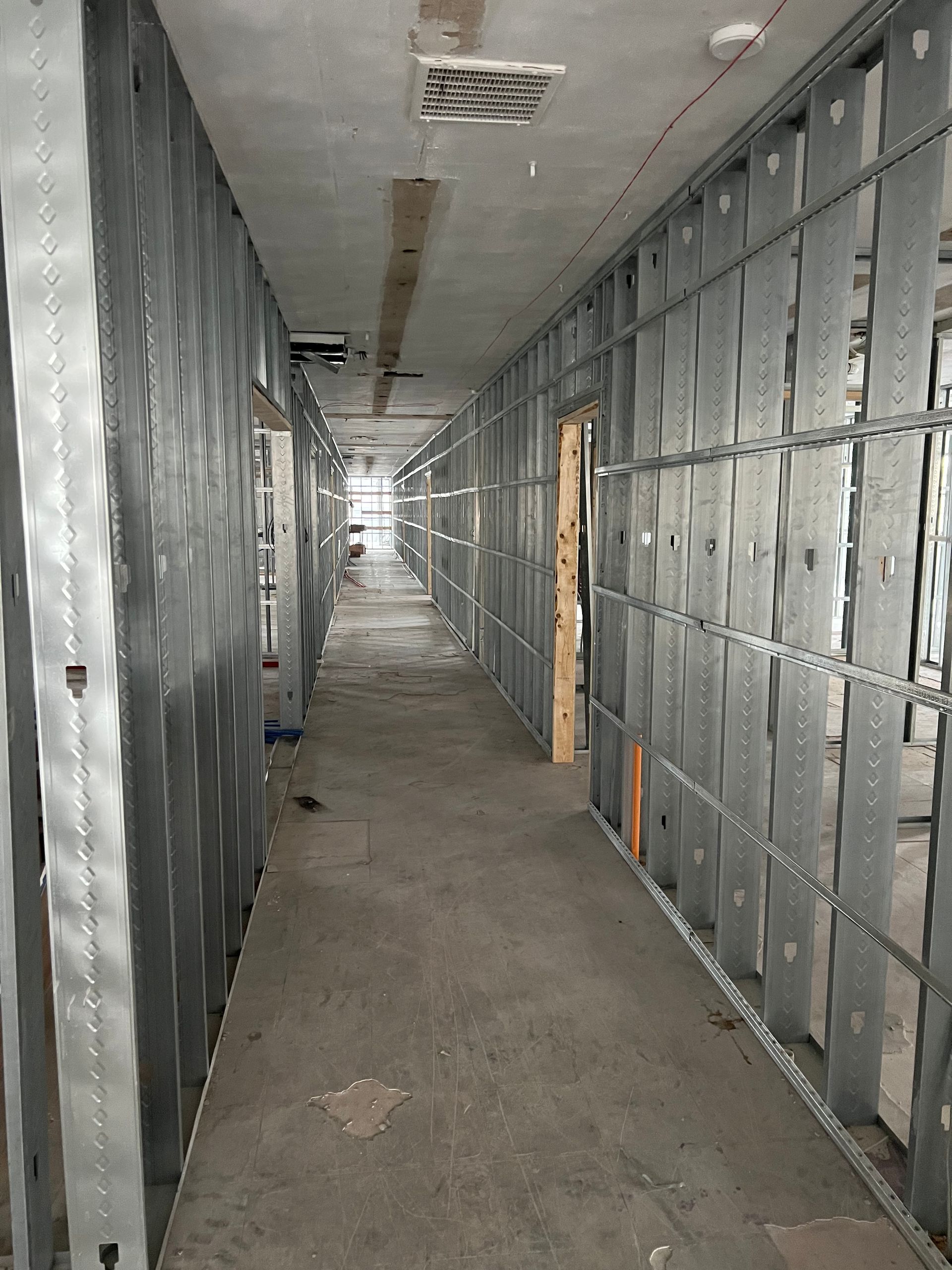 Metal-framed hallway under construction; exposed studs line the walls. Concrete floor.