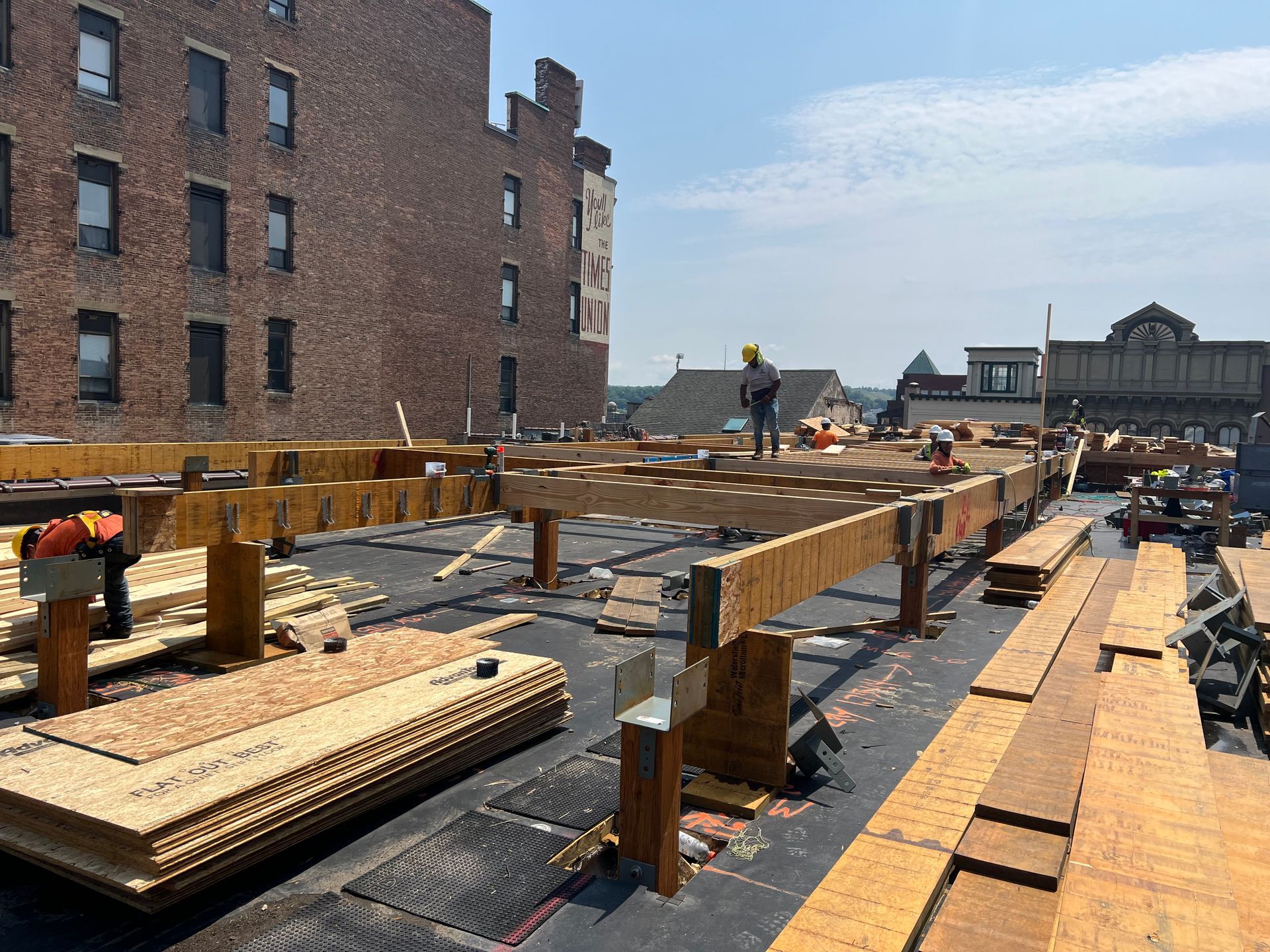 Construction workers on a rooftop, building a new structure with wooden beams and planks. Sunny day.