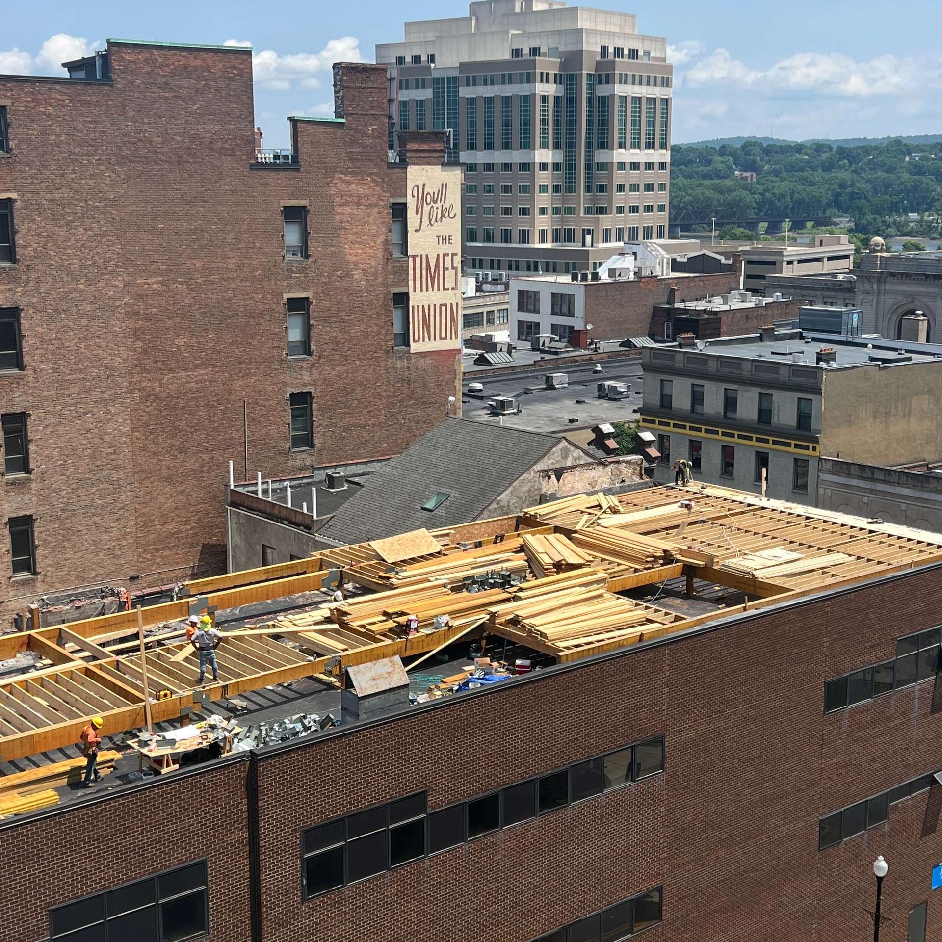 Cityscape with construction on a low roof, brick buildings, and a tall white building in the background.