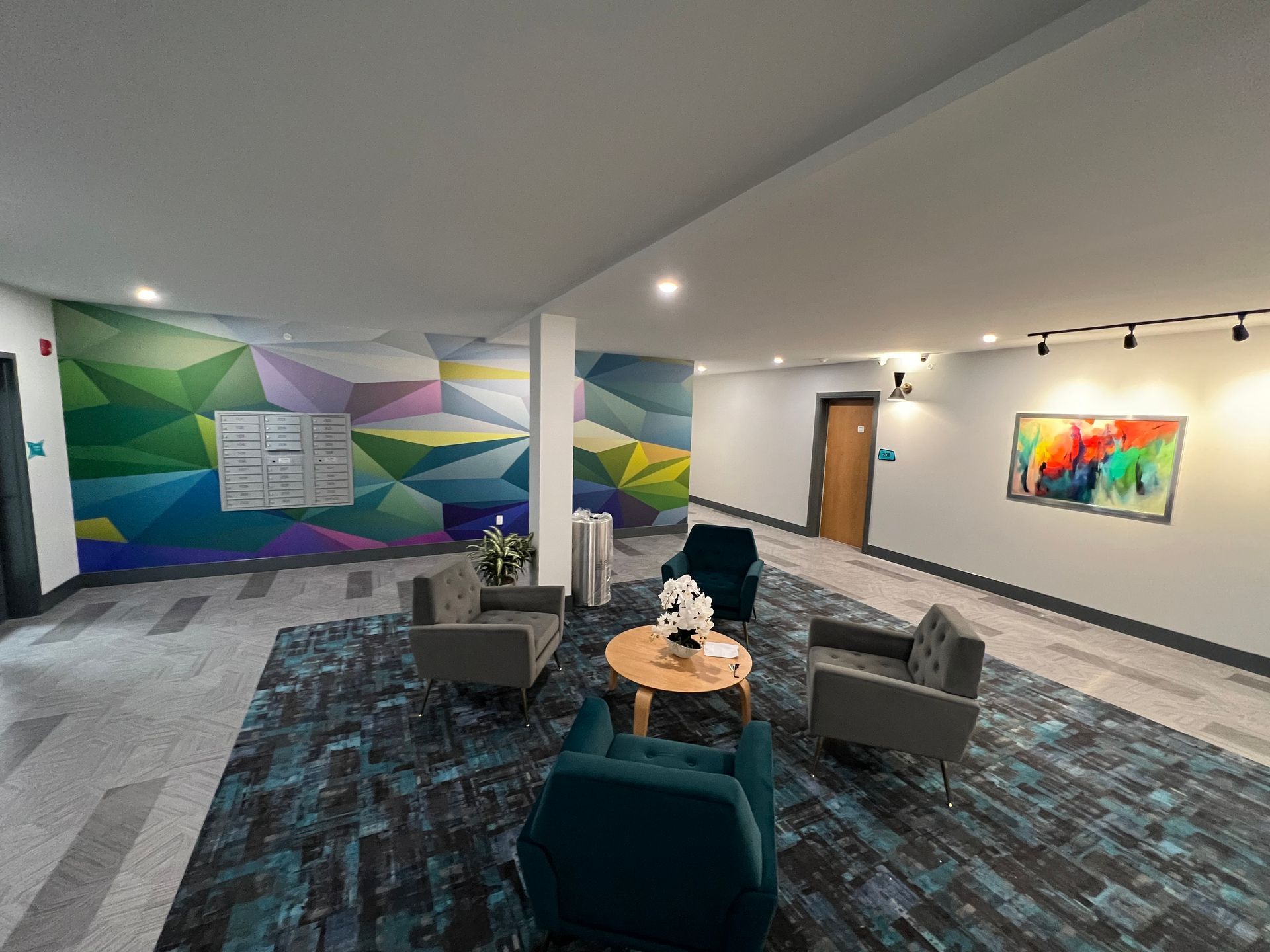Lobby with geometric mural, seating area, art, and doors. Teal and gray color scheme, modern design.