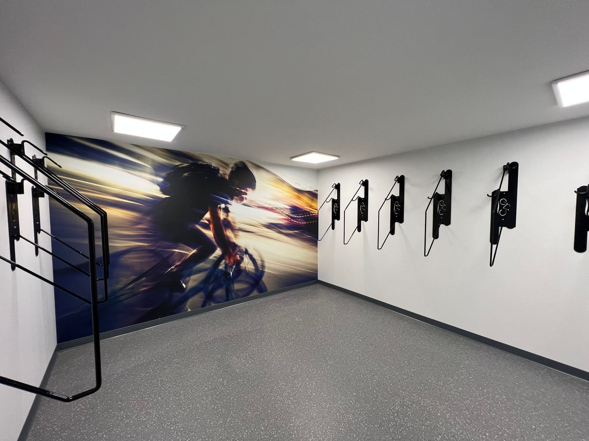 Bike storage room with black wall mounts, cycling mural, and gray floor.