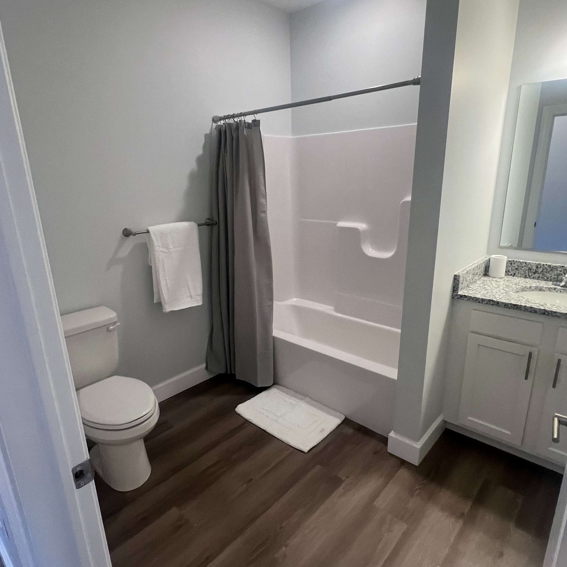 Bathroom with gray walls, white fixtures, dark wood-look floor, and a shower with a gray curtain.