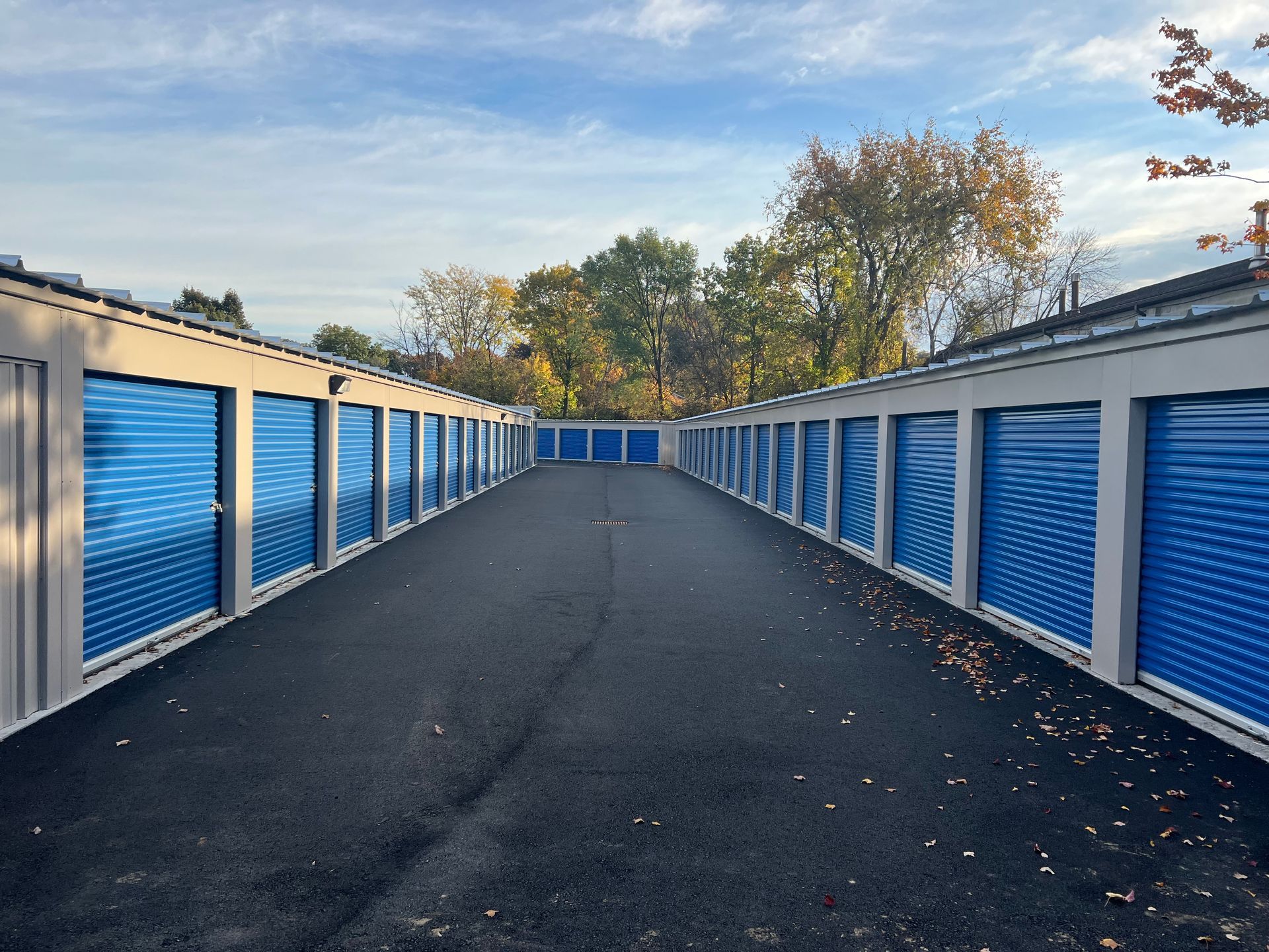 Rows of blue storage units with a black asphalt drive under a partly cloudy sky.