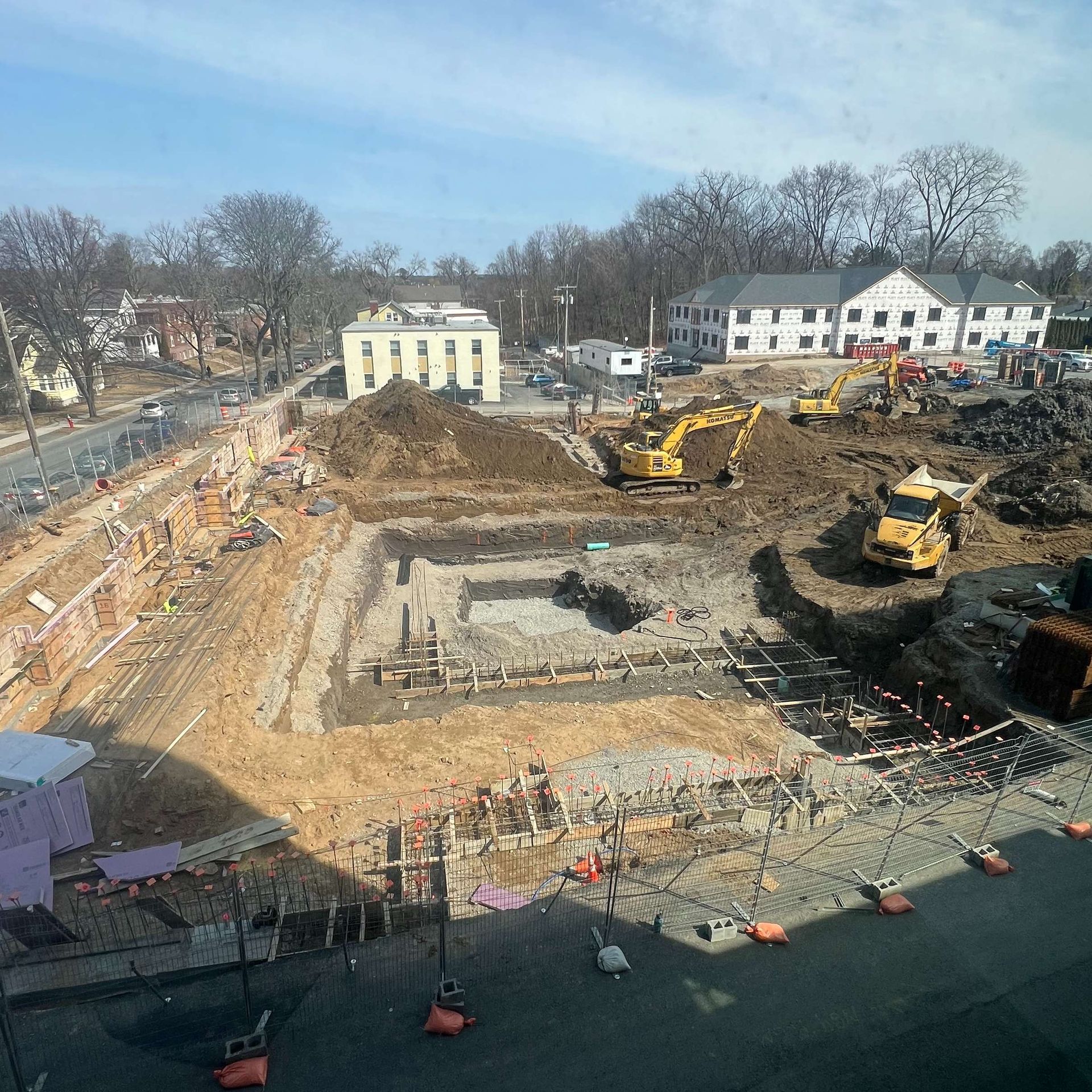 Construction site with excavators, dirt piles, and partially built foundations.
