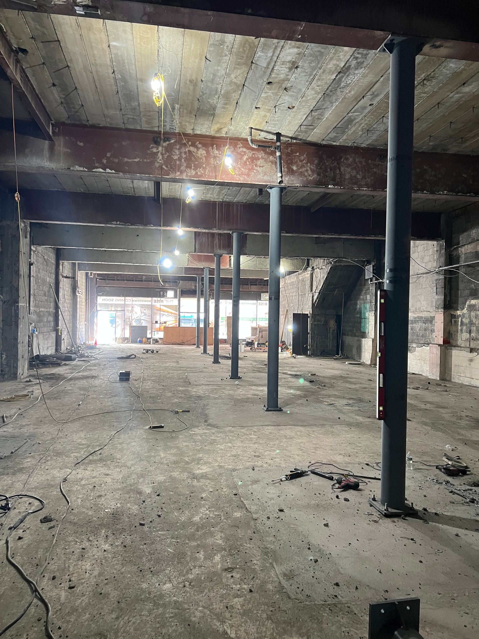 An interior view of a gutted building with exposed beams, support columns, and concrete flooring.