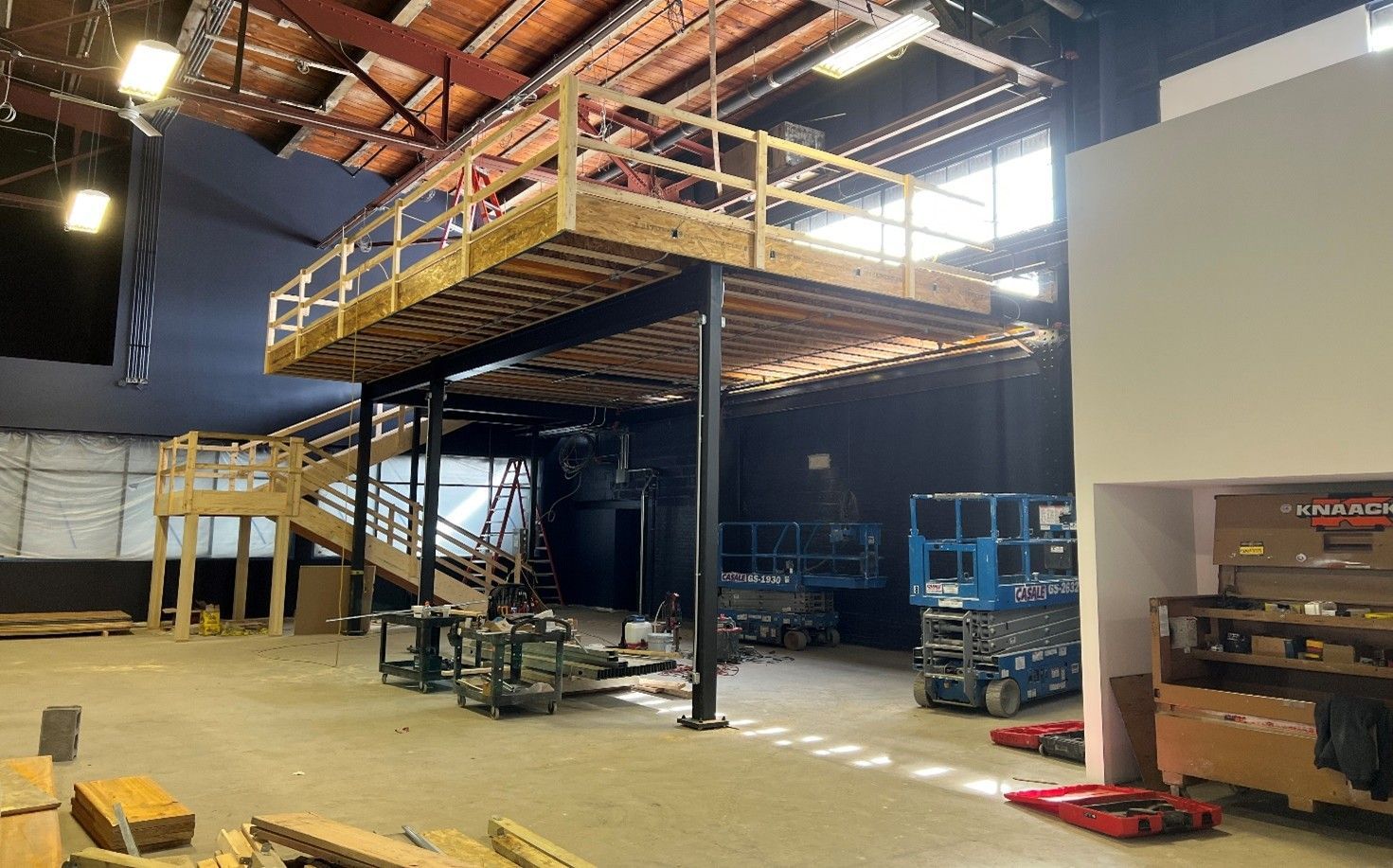Interior construction of a building with a wooden mezzanine, stairs, and exposed beams.