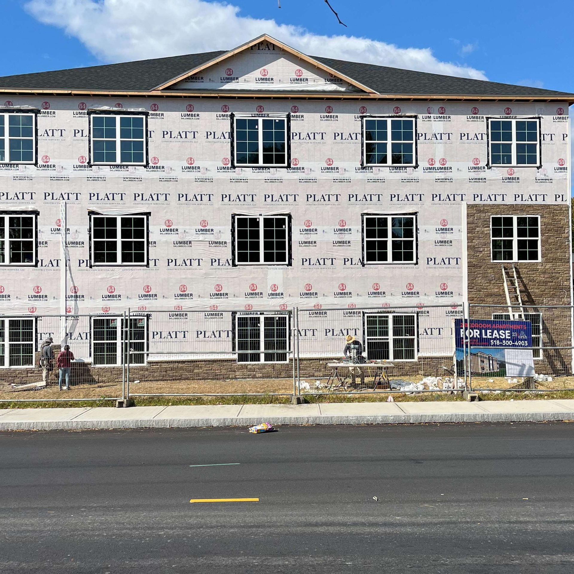 Building under construction with windows and brick facade, covered in protective material. Workers are present.
