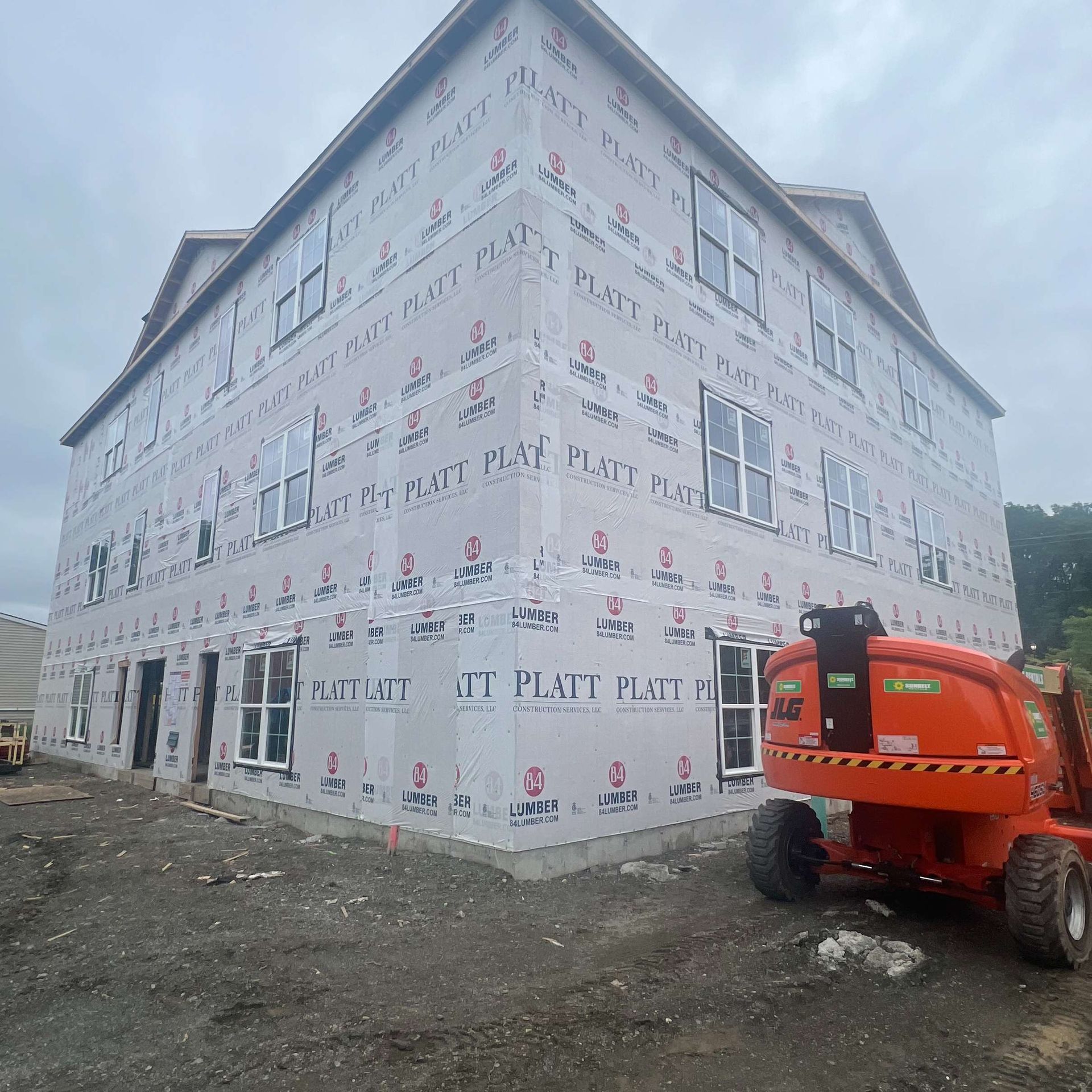 Building under construction, sheathing with wrap, windows installed. Orange lift. Gray sky.