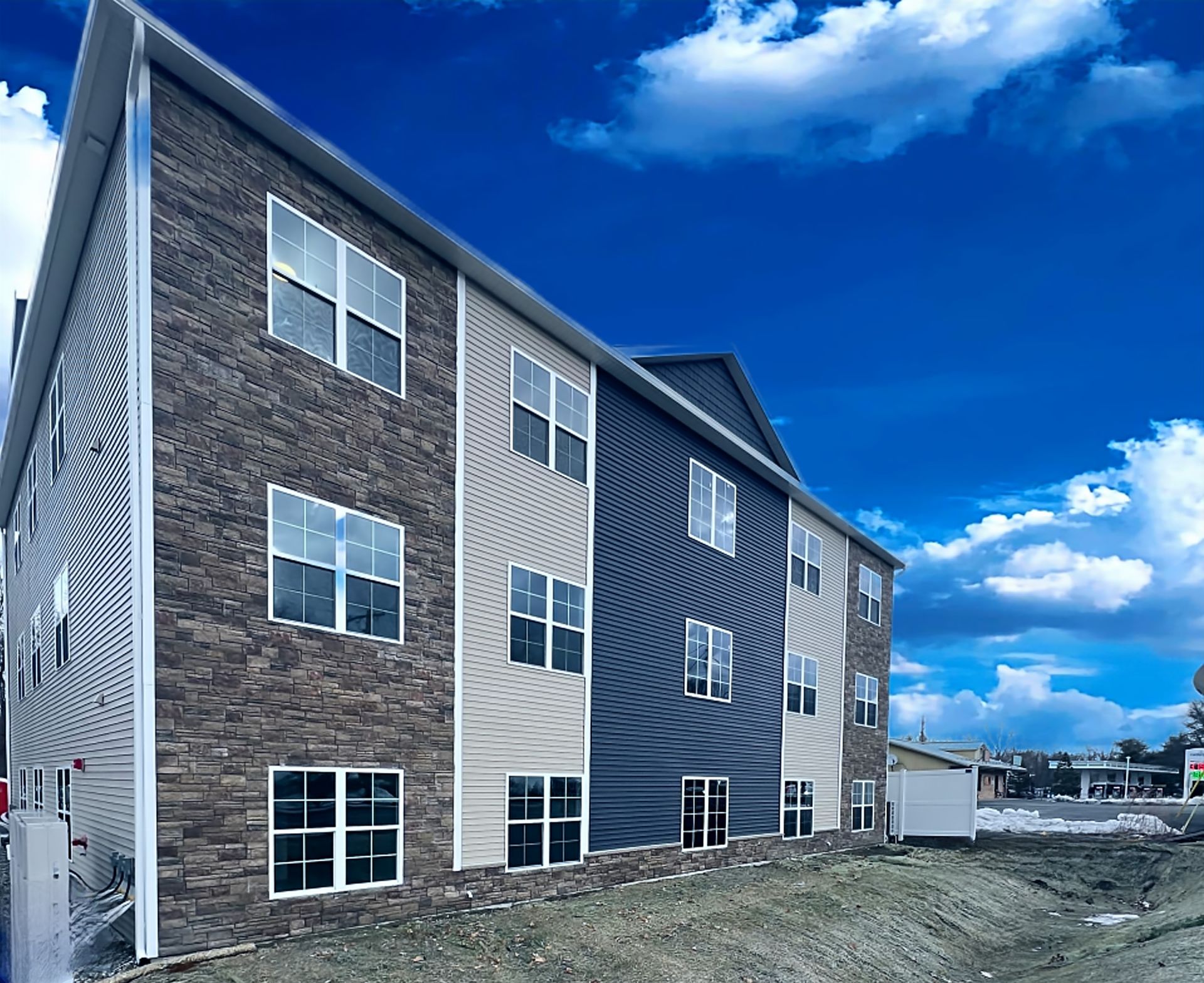 Apartment building with stone, beige, and blue siding against a cloudy blue sky.