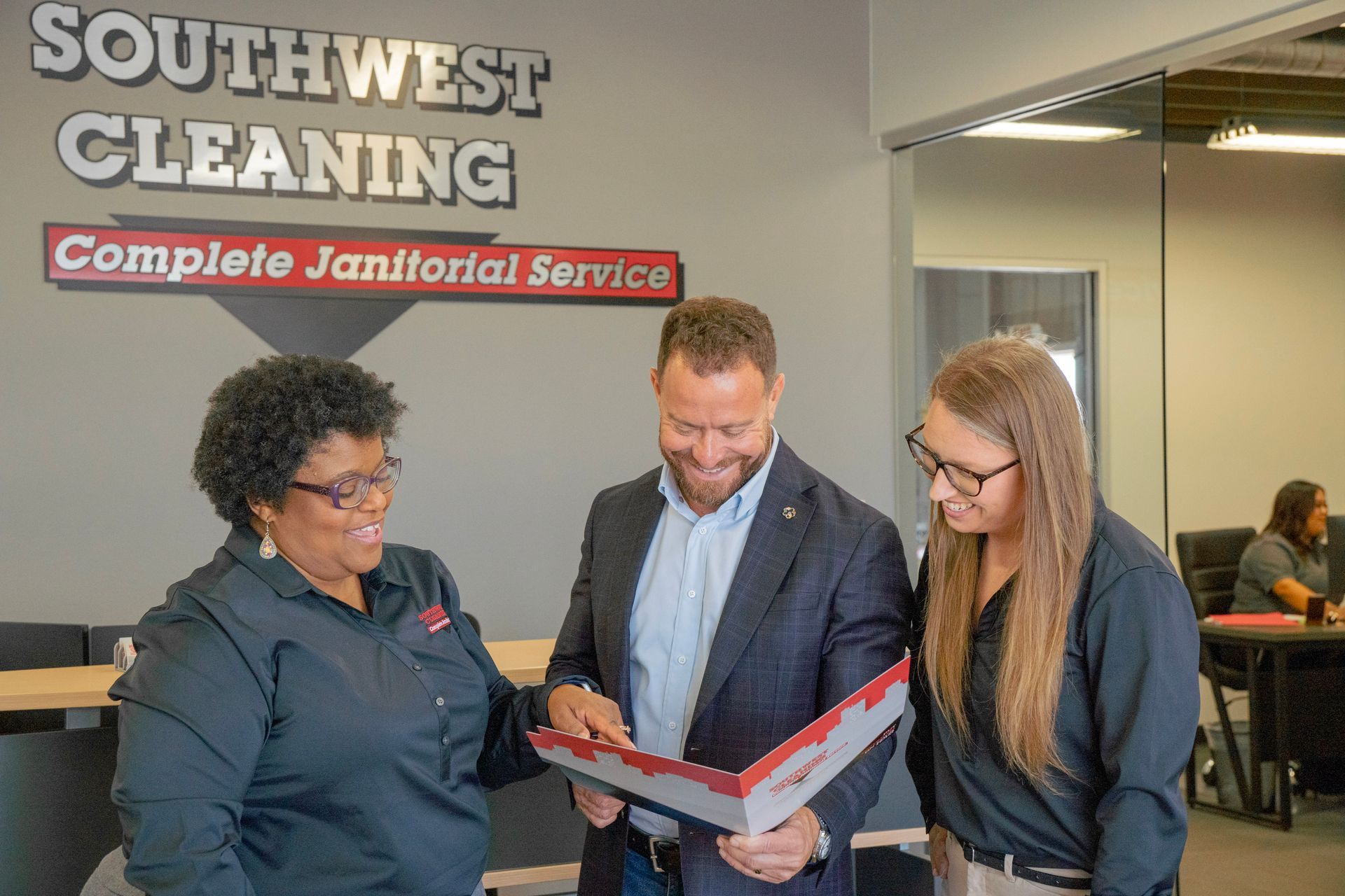 Three people reviewing a red folder in an office.