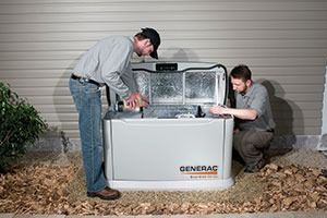 Two men installing a Generac generator outside a house. One opens the lid, other kneels.