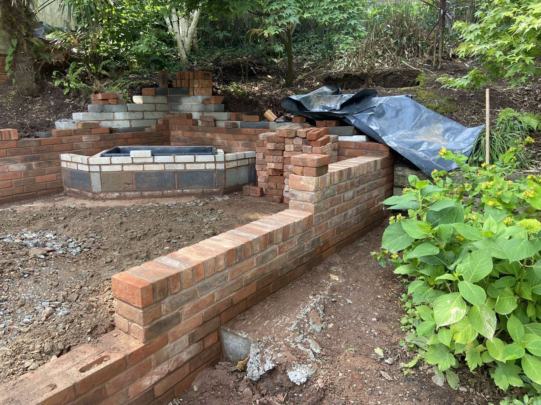 Brads Brick Wall Brick wall construction outside in garden by brad with bushes and trees in background and some tools