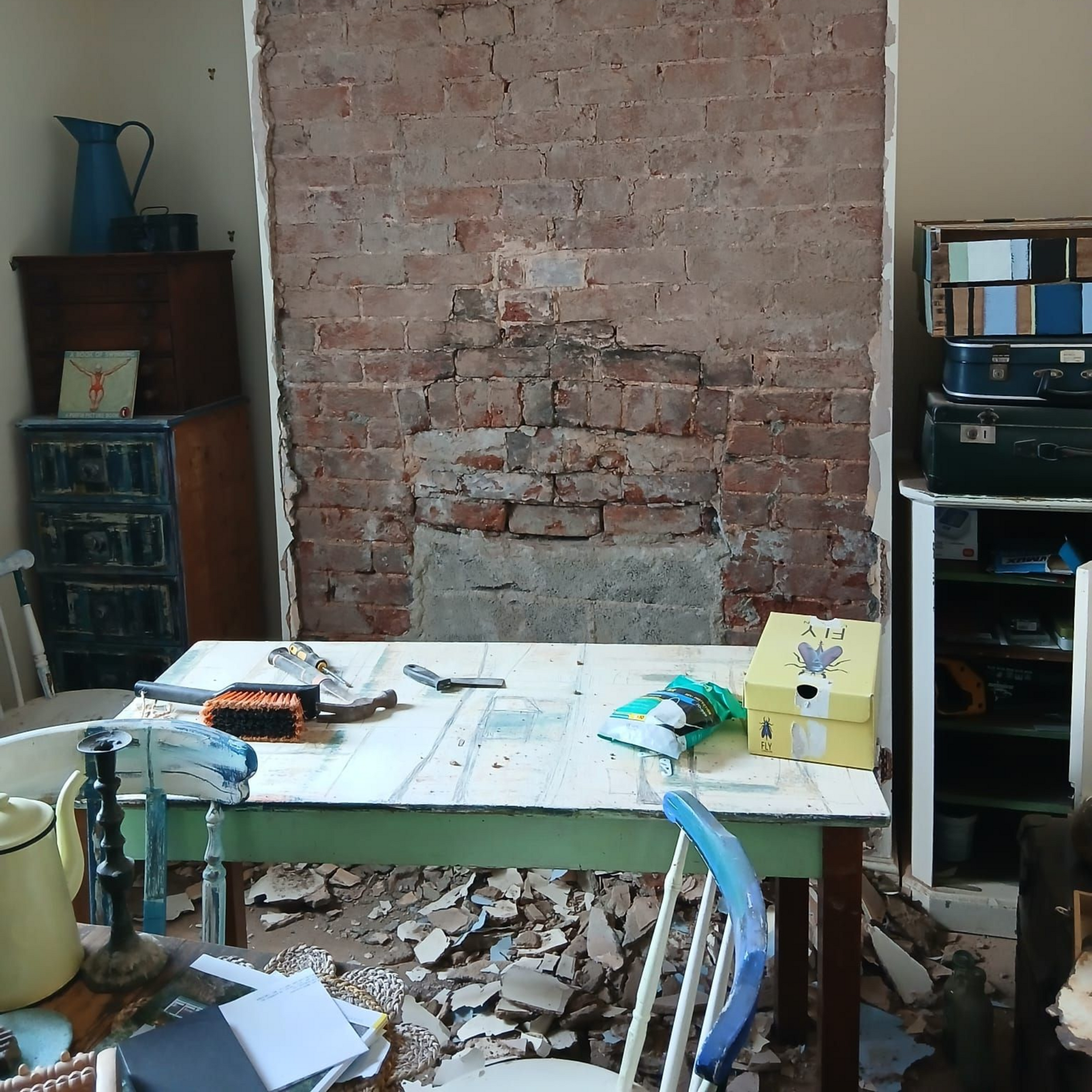 Room under renovation with exposed brick wall, table covered in tools and debris.