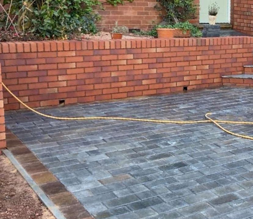 brick wall with pathing in driveway with sand on floor and bushes in background