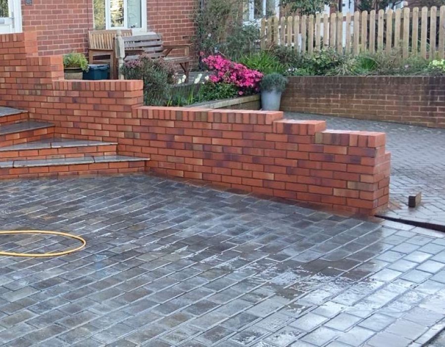 brick wall with pathing in driveway with sand on floor and bushes in background boundary wall