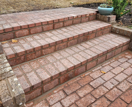 a patio with herringbone brickwork pattern on a steep slope with 2 white garage doors and a brick wall