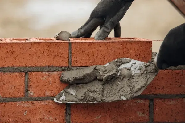 close up hand bricklaying mortar beds on clay bricks with black gloves on 