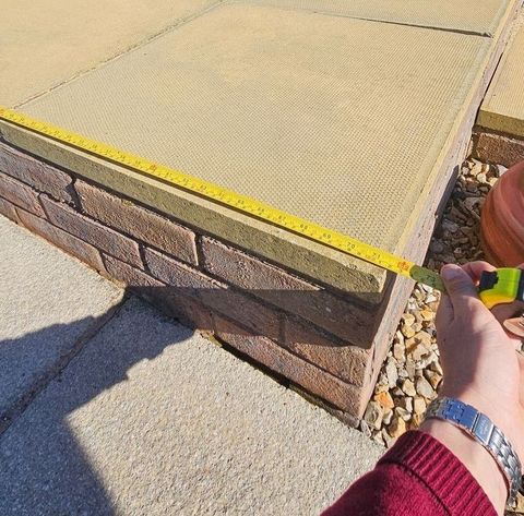 Tape measure over a patio on a sunny day by a man with a silver watch on