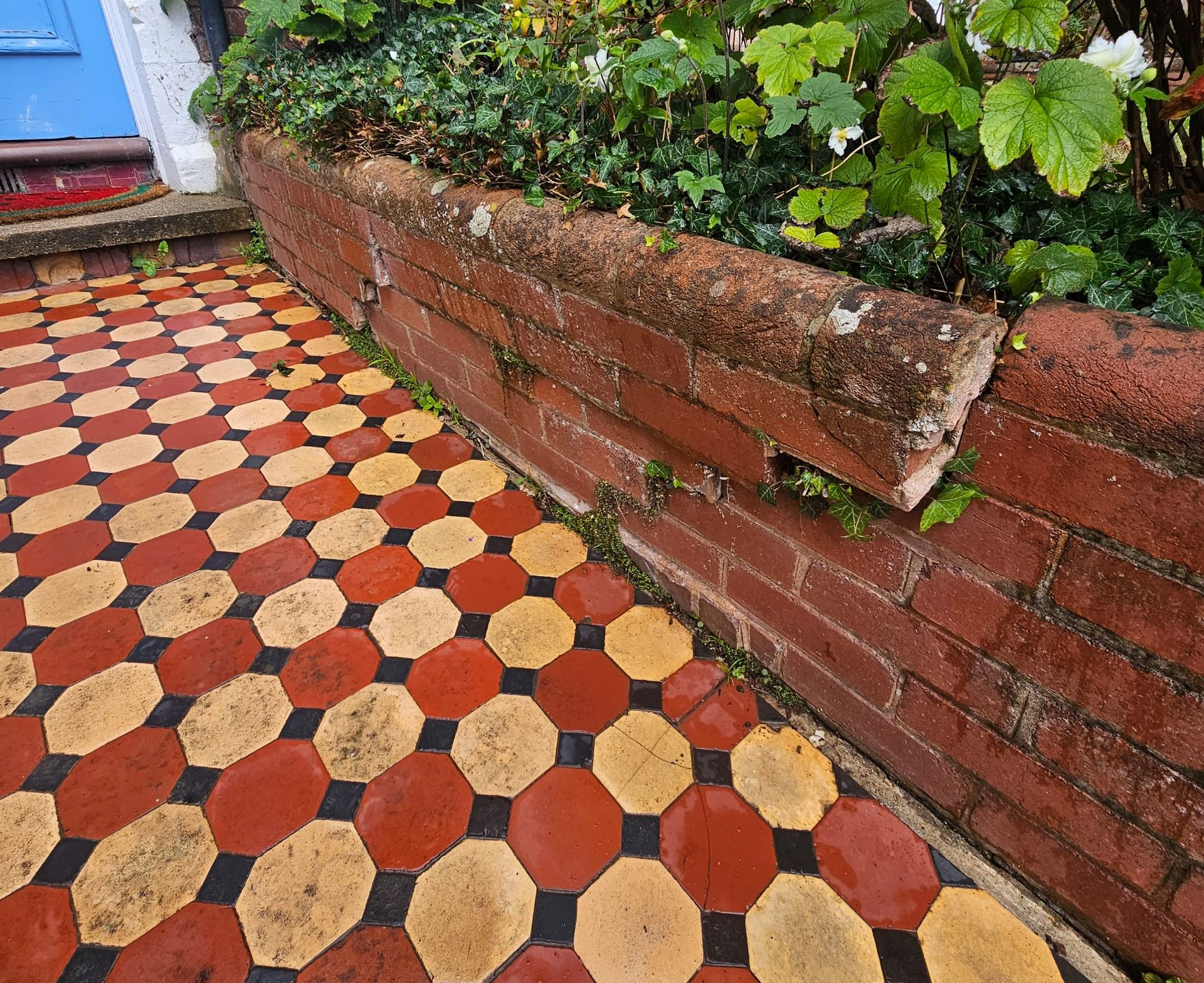 Brick wall with weathered cap, bordering a colorful patterned walkway and garden foliage.