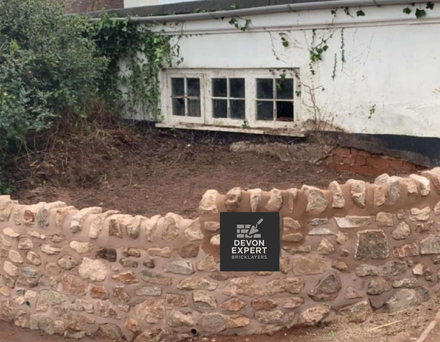 Brad retaining wall install for devon expert bricklayers made out of stone with white woodern window in background
