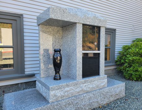A memorial with a black vase in front of a building.